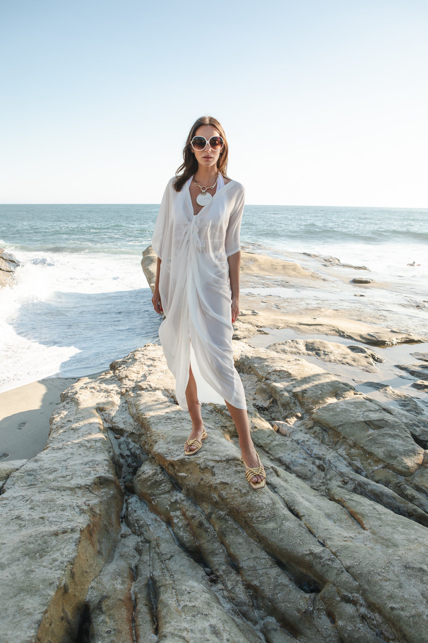 White semi sheer chiffon caftan. This solid color piece features a deep v-neck, batwing sleeve, a center drawstring for ruche styling, and ankle length hem. 