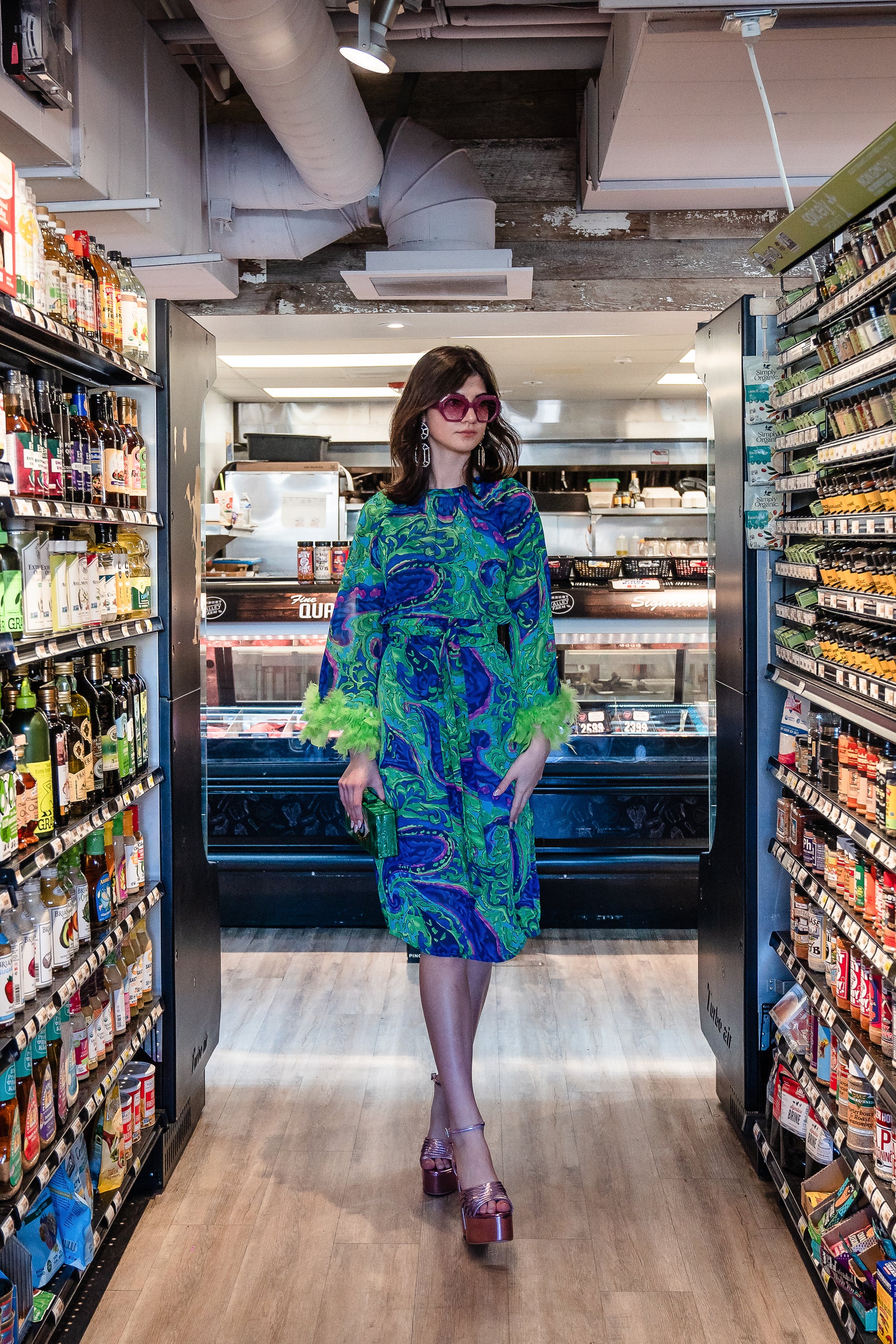 Funky fresh retro midi dress with royal blue and lime green abstract filigree swirl print with hints of aqua and fuchsia. The dress features a crew neck, keyhole detail at upper back, 3/4 bell sleeves with neon green feathers at cuff, a knee-length hem, and optional wrap tie for a cinched waist.