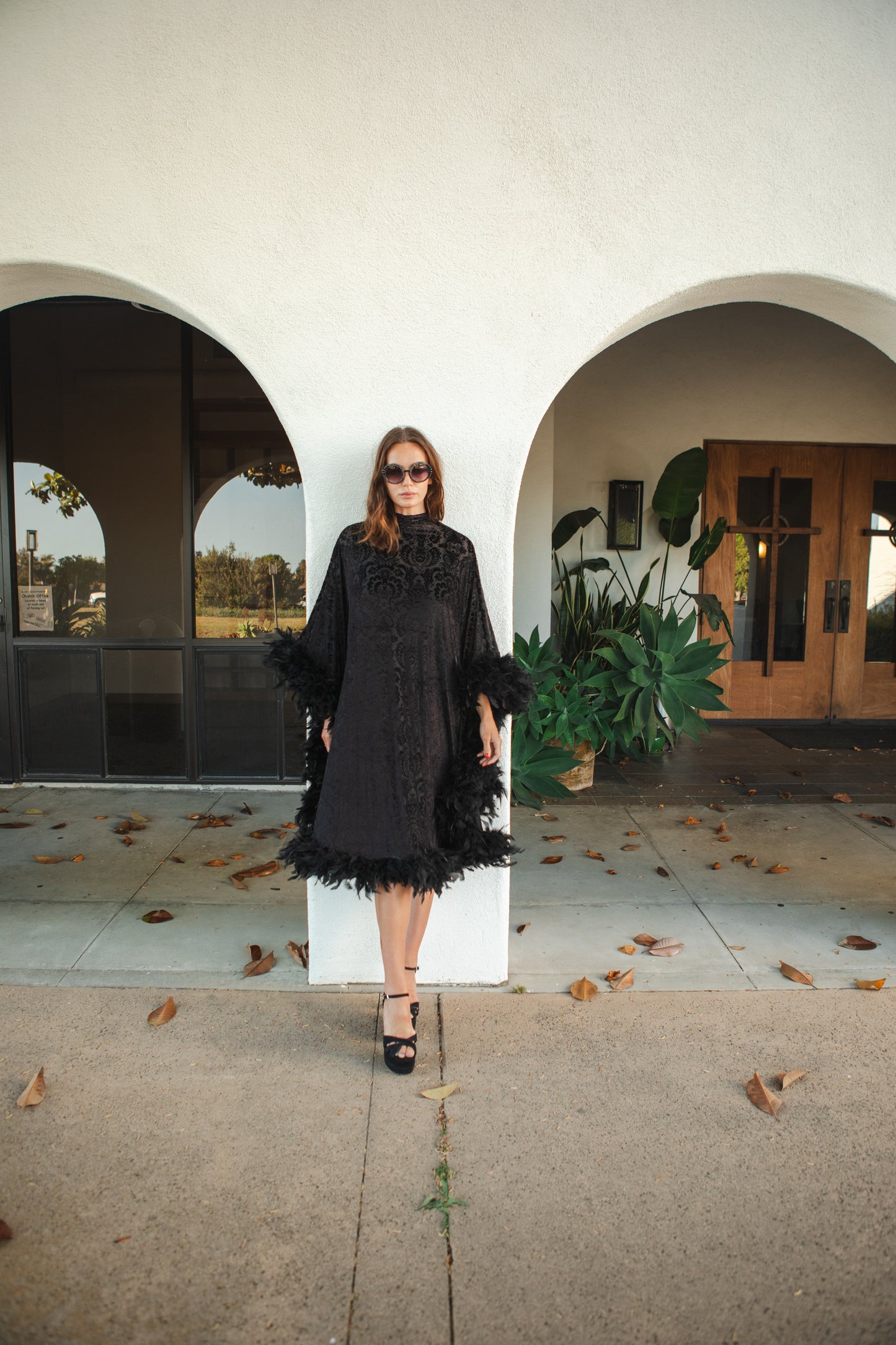 The Black Widow Mockneck Feather Caftan with slip. A darkly romantic, semi-sheer, black stretch velvet kaftan with a vintage-inspired, ornamental burnout pattern and soft black feather border along sleeves and hem. A gothic bohemian dress inspired by Old Hollywood glam.