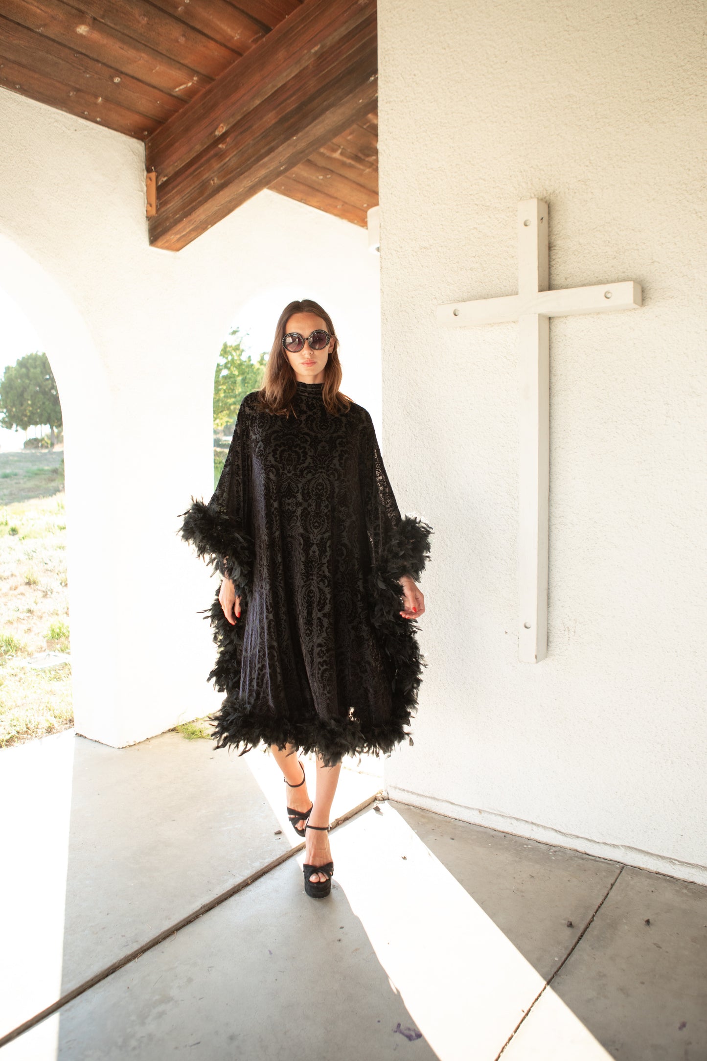 The Black Widow Mockneck Feather Caftan with slip. A darkly romantic, semi-sheer, black stretch velvet kaftan with a vintage-inspired, ornamental burnout pattern and soft black feather border along sleeves and hem. A gothic bohemian dress inspired by Old Hollywood glam.