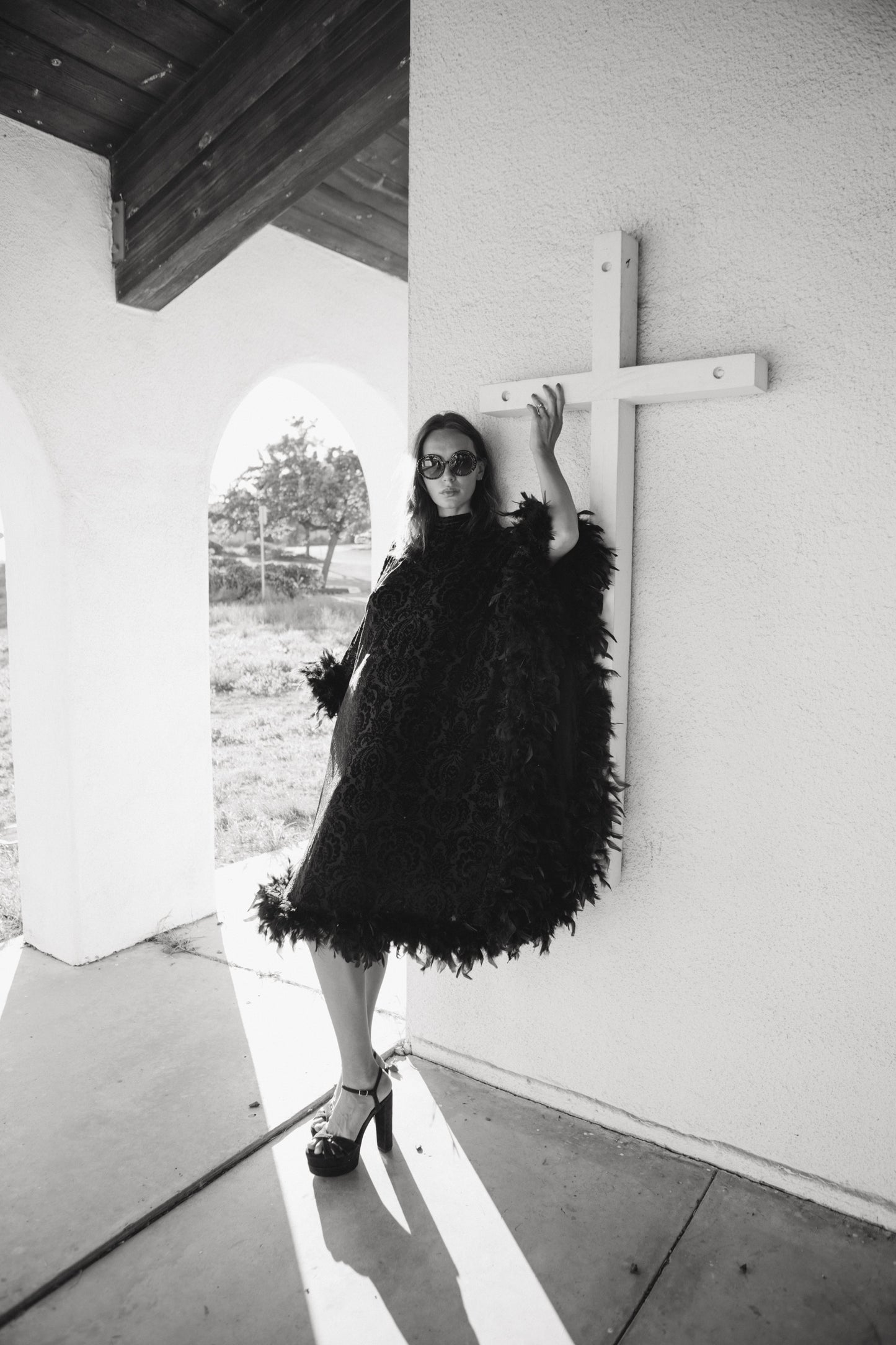 The Black Widow Mockneck Feather Caftan with slip. A darkly romantic, semi-sheer, black stretch velvet kaftan with a vintage-inspired, ornamental burnout pattern and soft black feather border along sleeves and hem. A gothic bohemian dress inspired by Old Hollywood glam.
