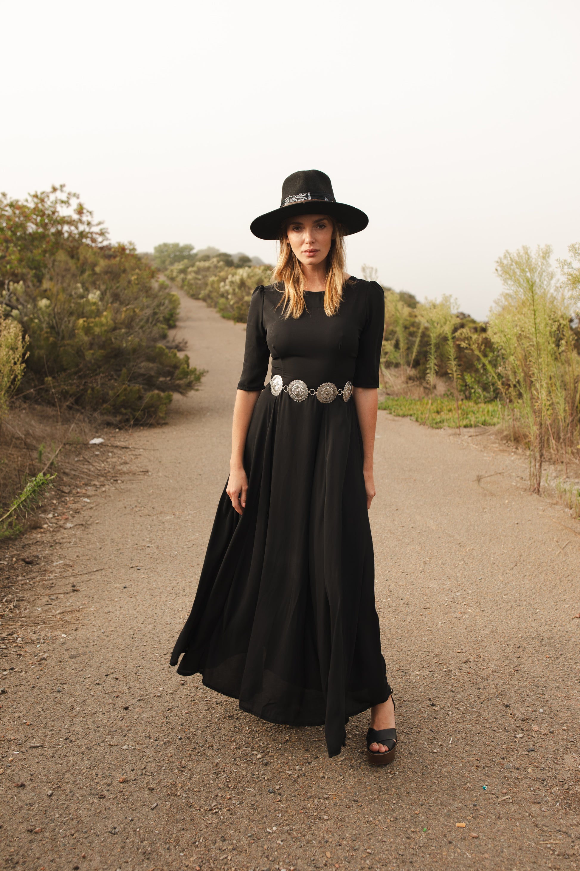 Jennafer Grace solid black maxi dress features princess seamed skirts and pockets. The dress has an invisible zipper and high/low neck options you can wear it multiple ways. Fitted torso with elbow length sleeves and ankle hem.
