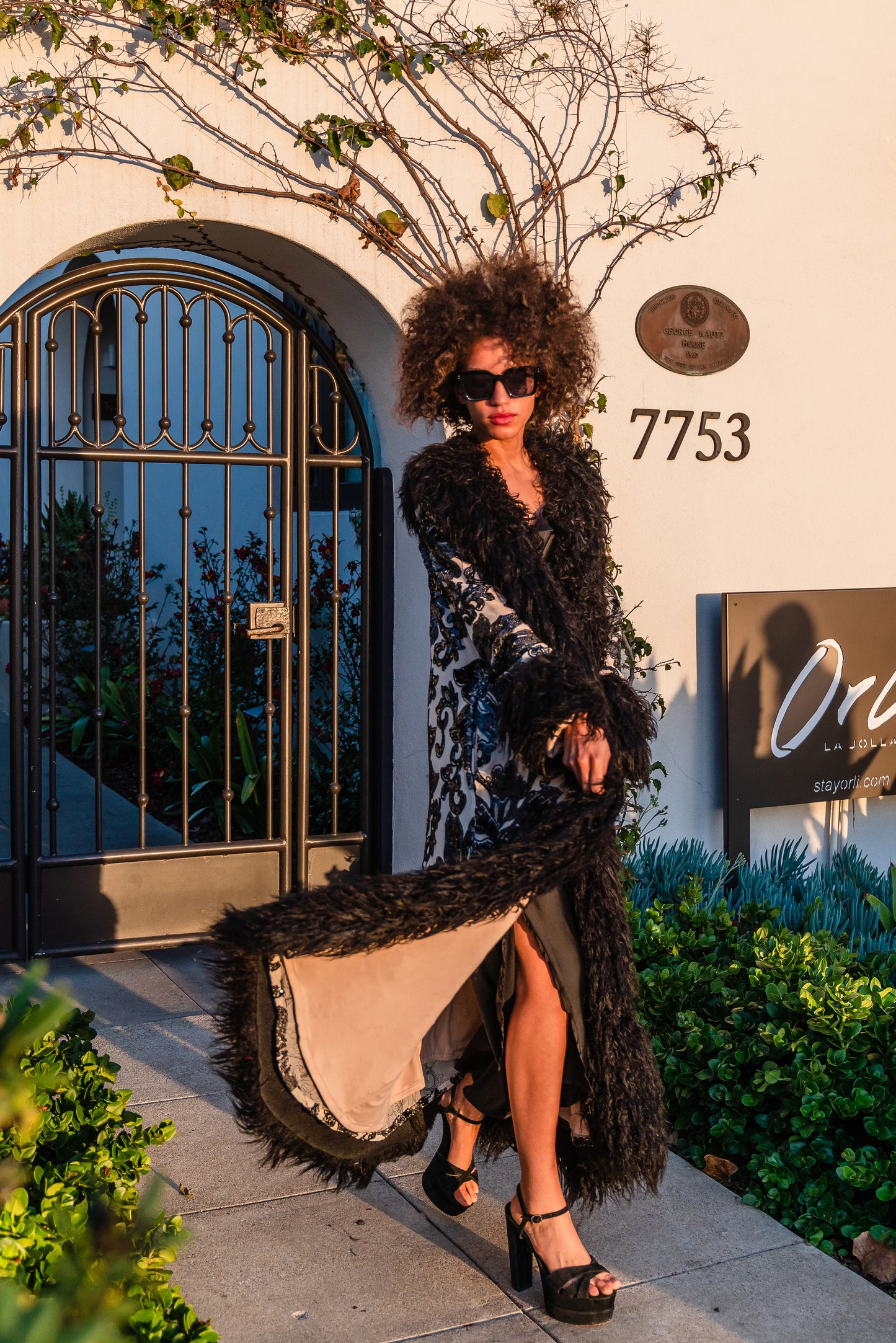 A floor length coat made of nude mesh with black sequins in a floral patter. The coat is lined around the collar, down the opening and around the hem in fluffy black faux alpaca fur, the coat has pockets and a nude colored lining of bamboo jersey.