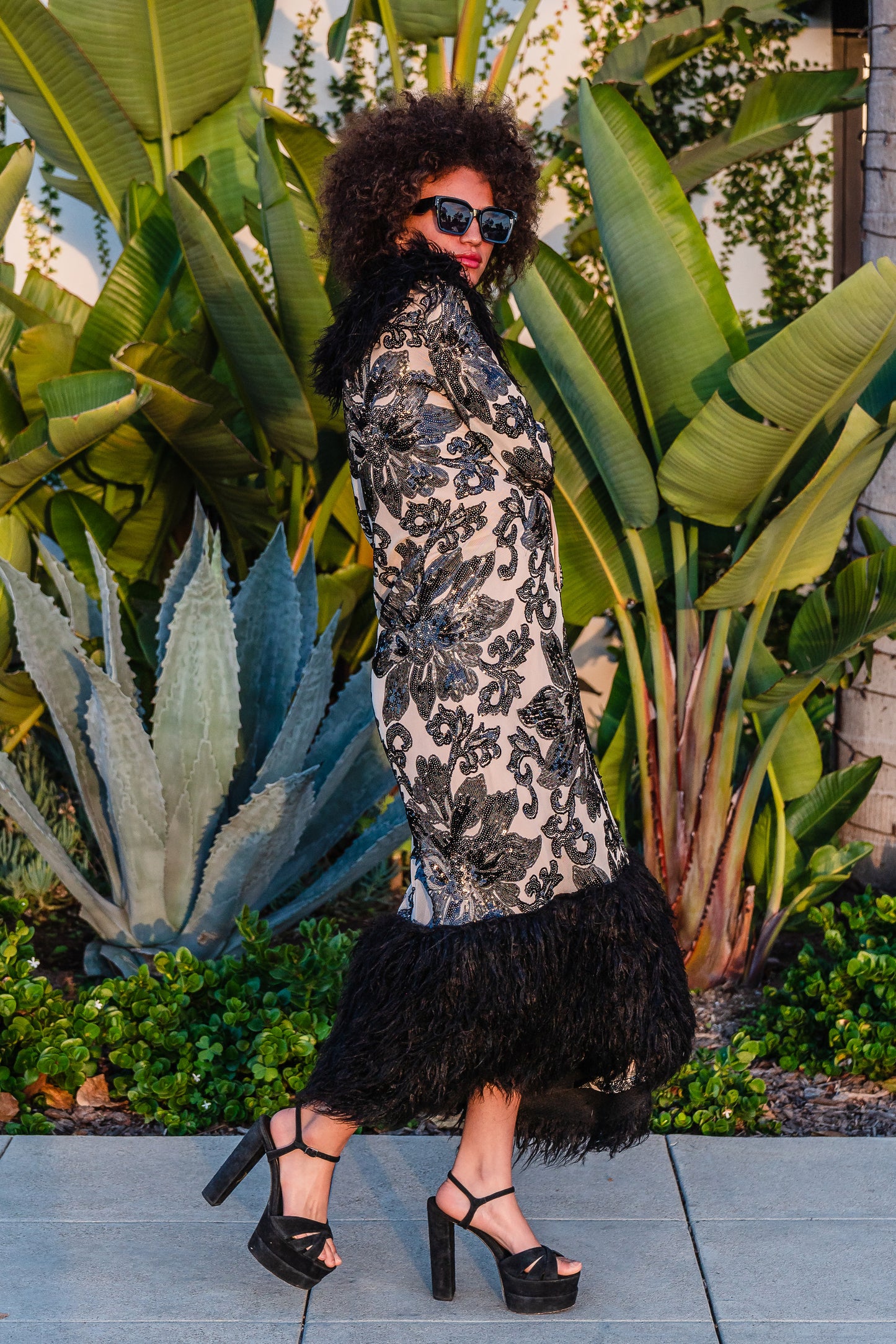 A floor length coat made of nude mesh with black sequins in a floral patter. The coat is lined around the collar, down the opening and around the hem in fluffy black faux alpaca fur, the coat has pockets and a nude colored lining of bamboo jersey.