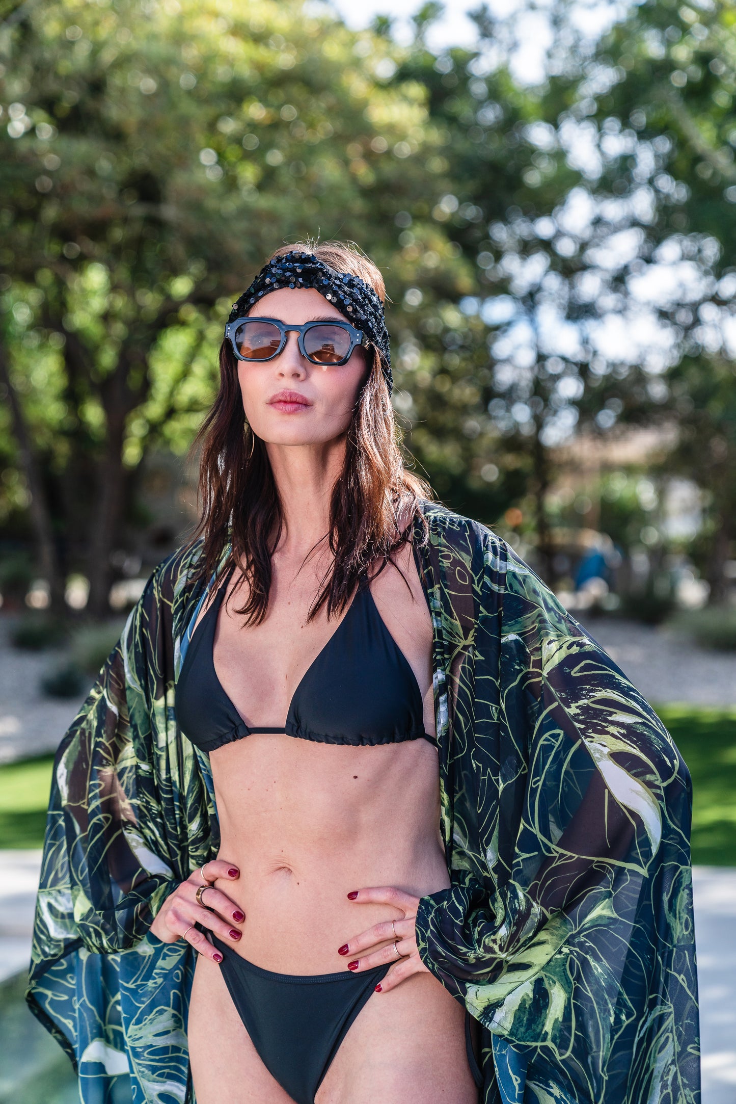 Model wears black chiffon Kimono with varying green palm leaf print. The kimono has classic wide kimono sleeves and lands at midi length. Kimono has a matching tie belt.