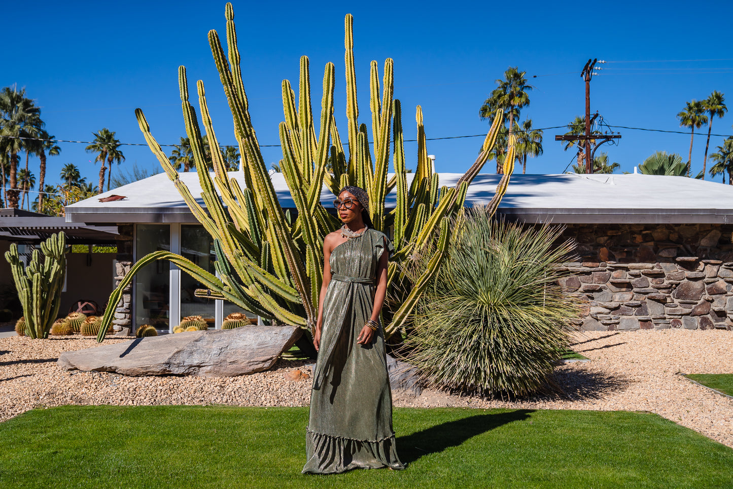 Model wears green jersey one shouldered floor length dress, the dress has a ruffle around the neckline and is dotted with metallic gold foiled dots.