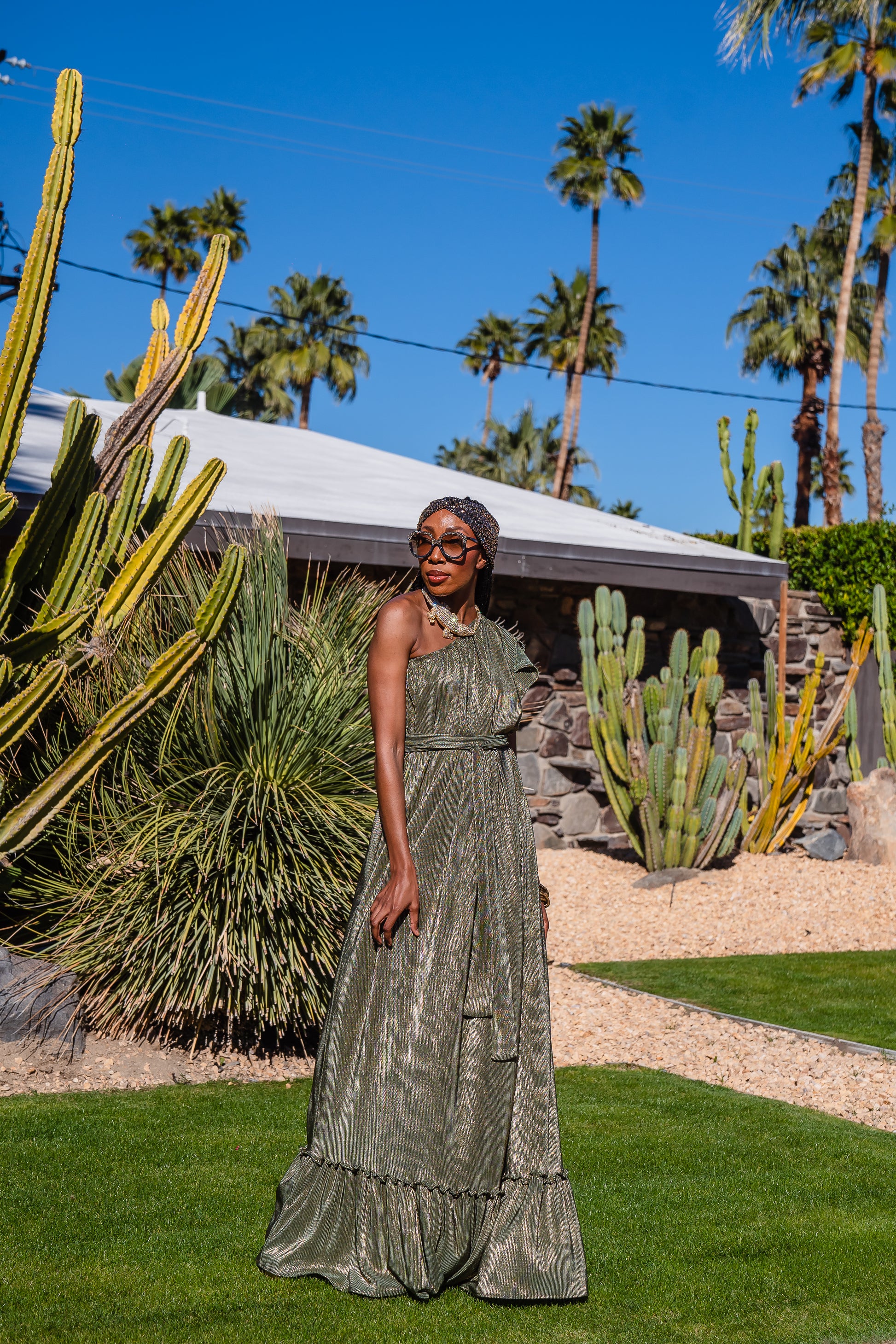Model wears green jersey one shouldered floor length dress, the dress has a ruffle around the neckline and is dotted with metallic gold foiled dots.
