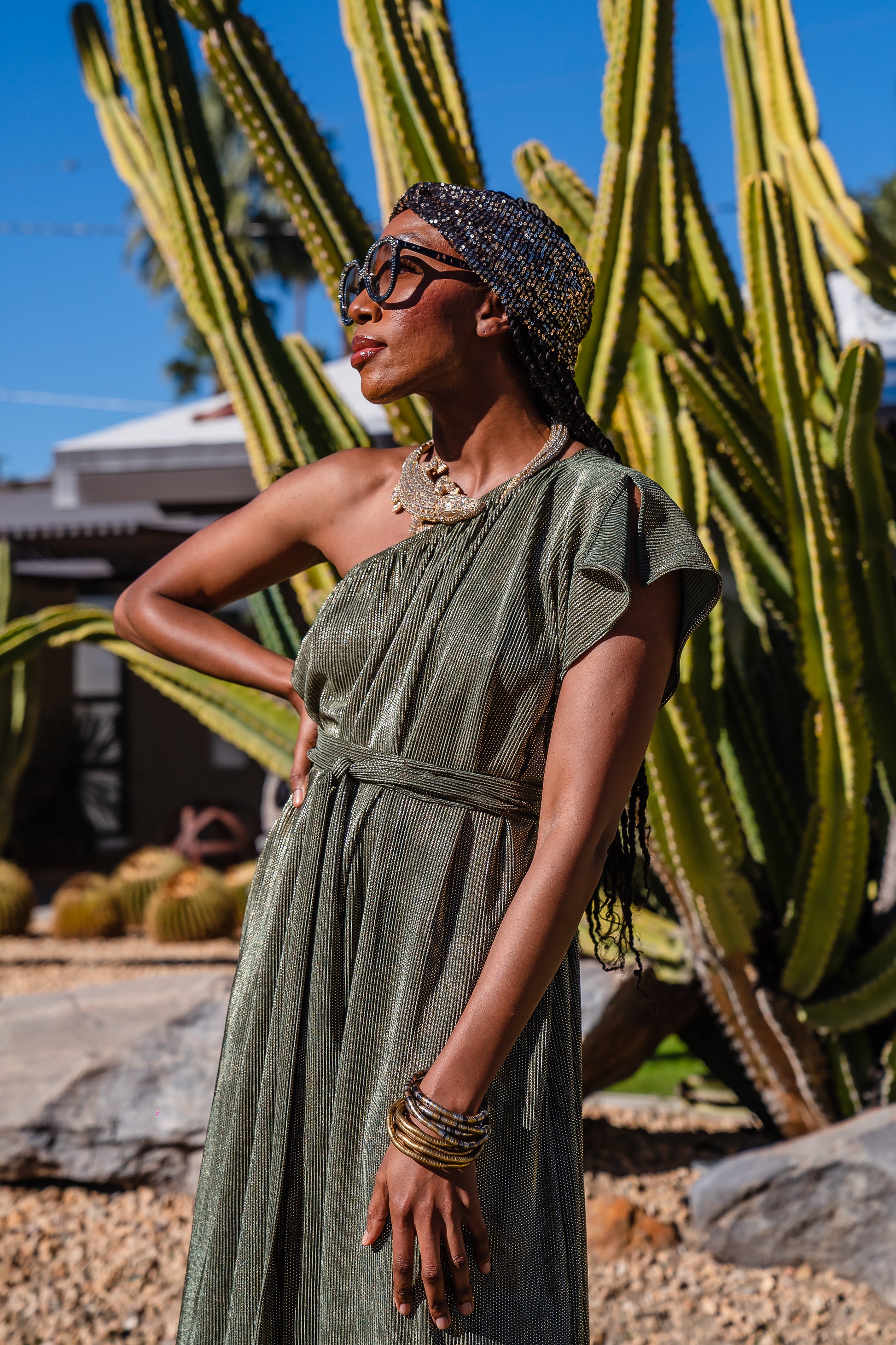 Model wears green jersey one shouldered floor length dress, the dress has a ruffle around the neckline and is dotted with metallic gold foiled dots.