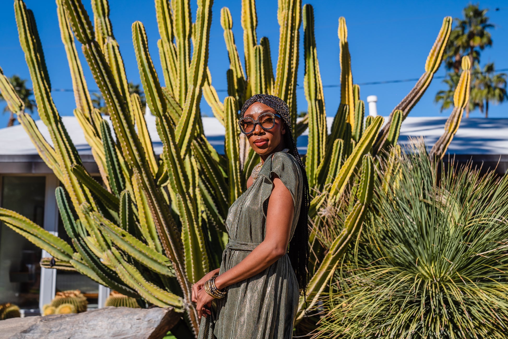 Model wears green jersey one shouldered floor length dress, the dress has a ruffle around the neckline and is dotted with metallic gold foiled dots.