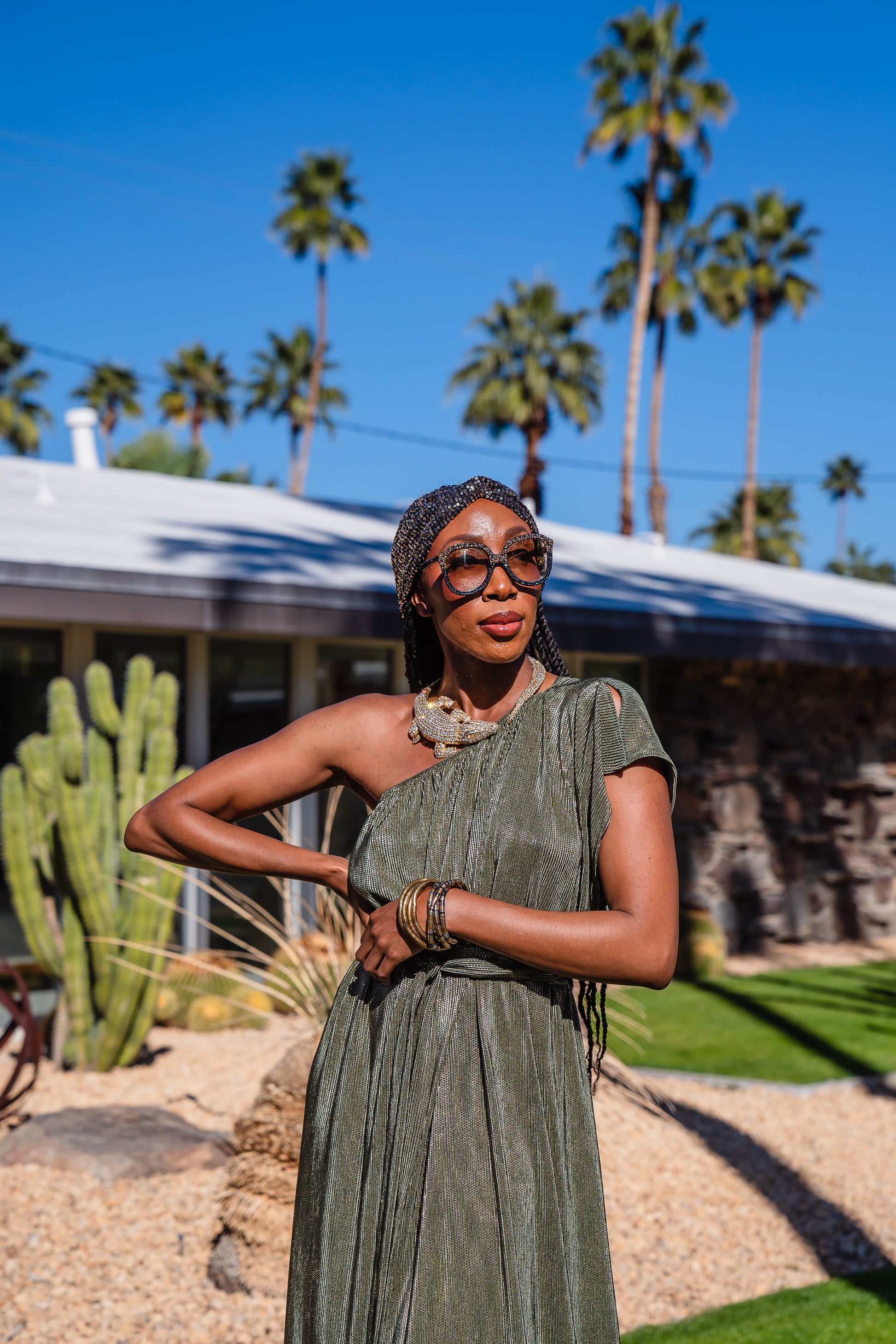 Model wears green jersey one shouldered floor length dress, the dress has a ruffle around the neckline and is dotted with metallic gold foiled dots.