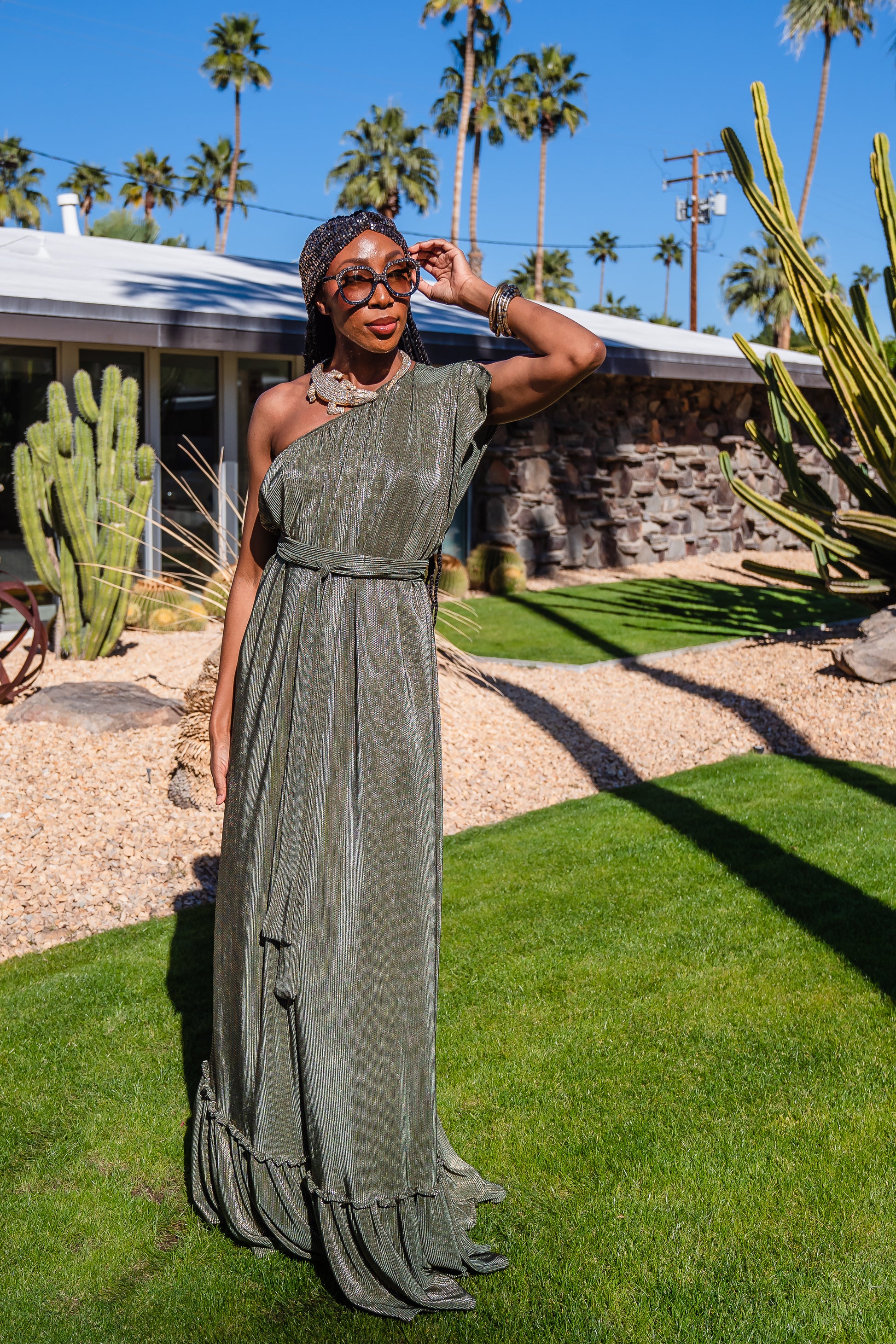 Model wears green jersey one shouldered floor length dress, the dress has a ruffle around the neckline and is dotted with metallic gold foiled dots.