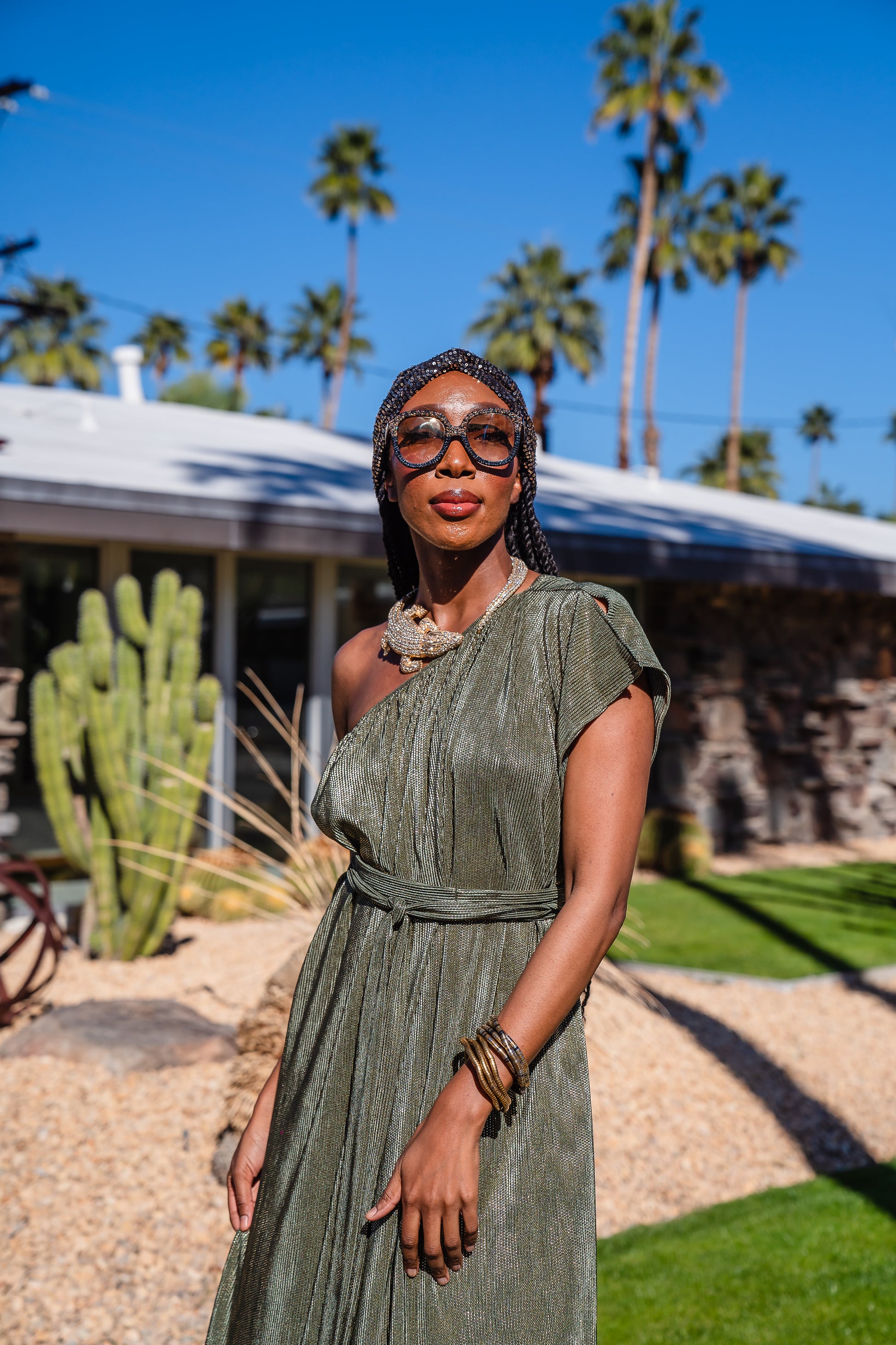 Model wears green jersey one shouldered floor length dress, the dress has a ruffle around the neckline and is dotted with metallic gold foiled dots.