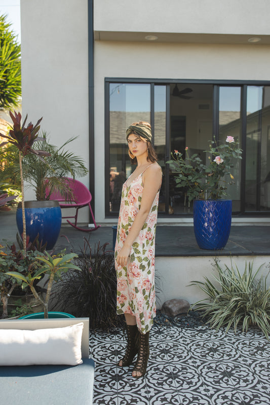 Midi slip dress with an ivory base color, adorned with floral rose print pattern featuring shades of green and pink. It features slender straps with a straight silhouette and relaxed fix, allowing for a beautiful drape and flowy movement. It's designed for a light, airy feel, suitable for warm weather or layered for cooler days.