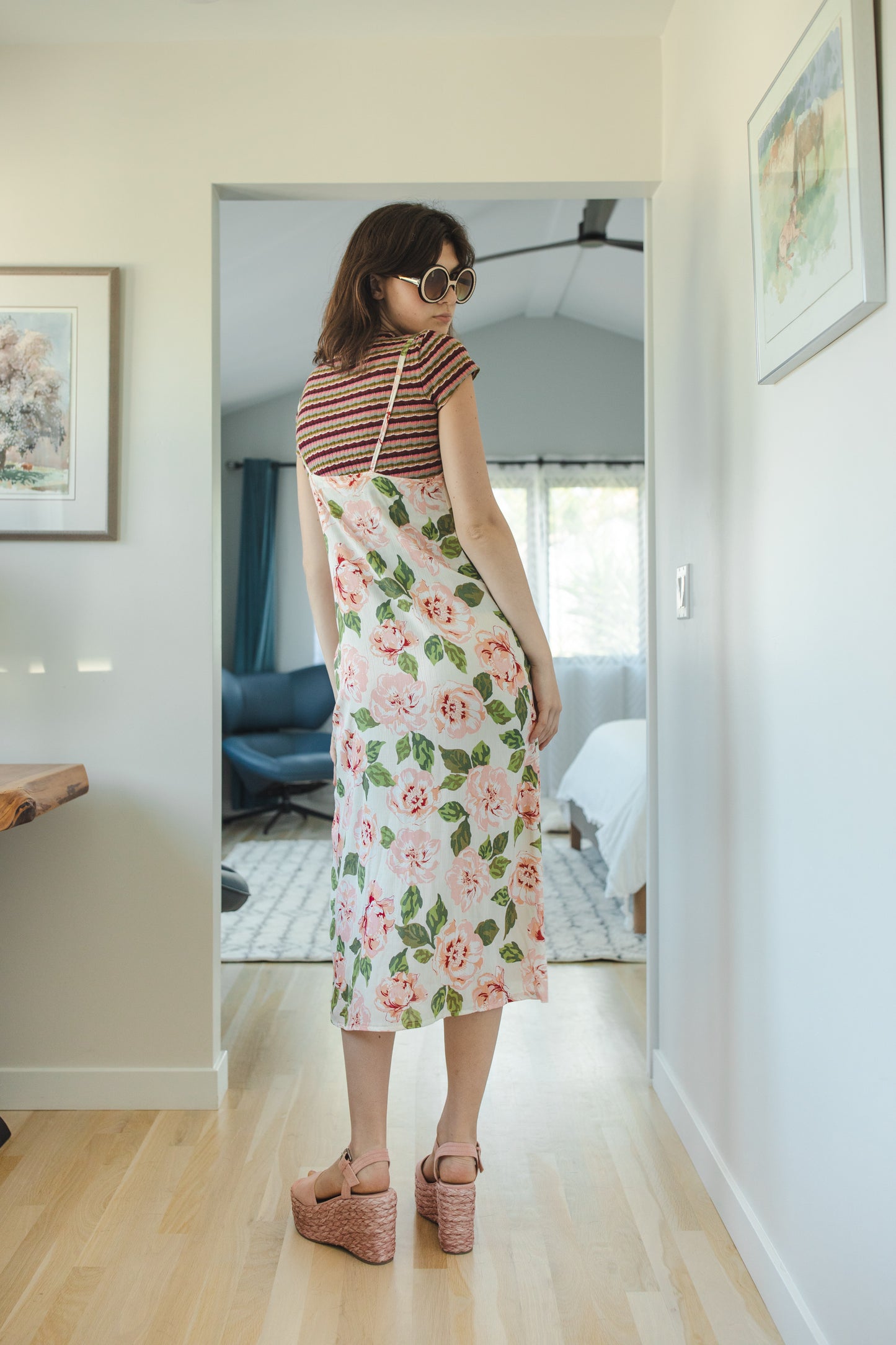 Midi slip dress with an ivory base color, adorned with floral rose print pattern featuring shades of green and pink. It features slender straps with a straight silhouette and relaxed fix, allowing for a beautiful drape and flowy movement. It's designed for a light, airy feel, suitable for warm weather or layered for cooler days.