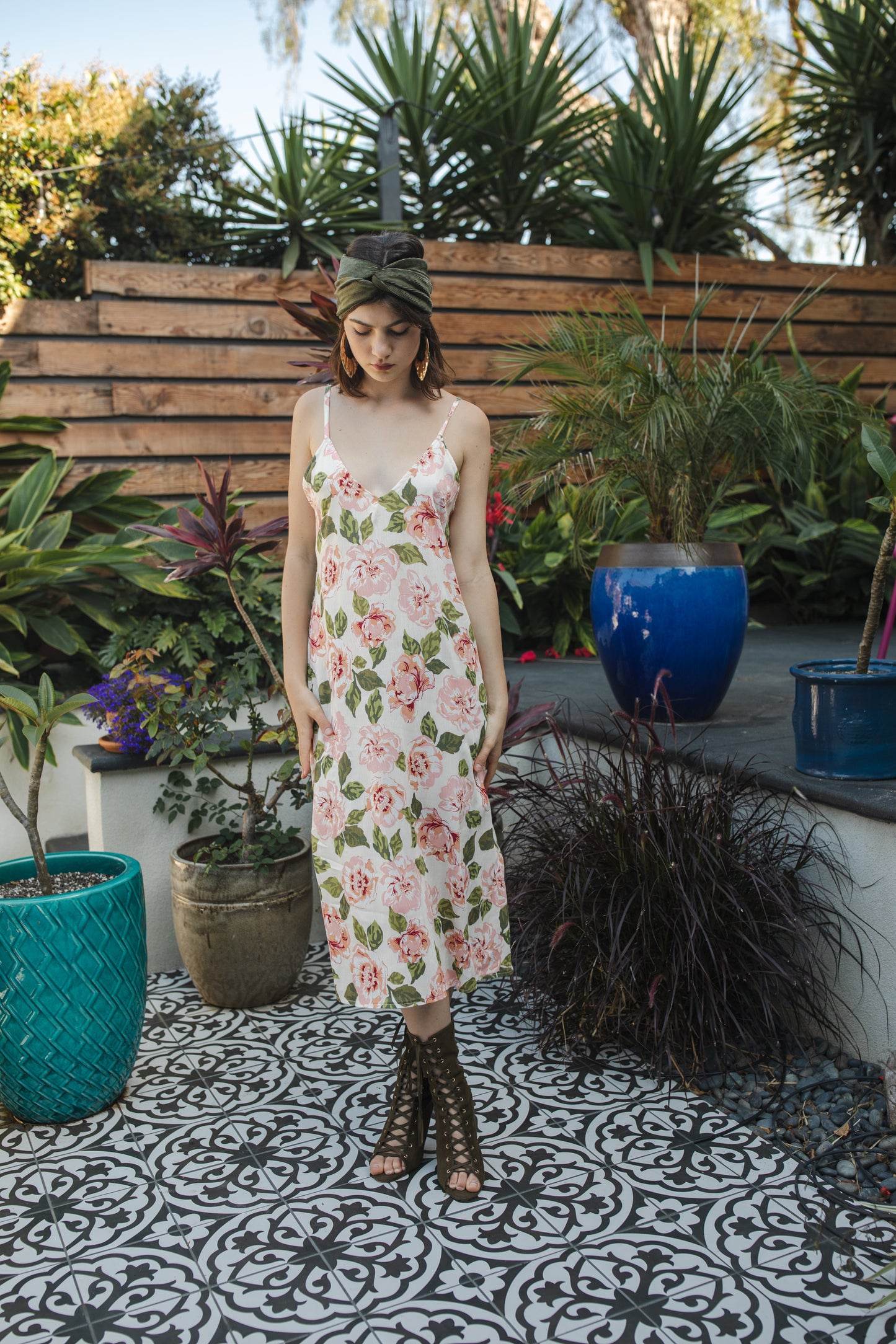 Midi slip dress with an ivory base color, adorned with floral rose print pattern featuring shades of green and pink. It features slender straps with a straight silhouette and relaxed fix, allowing for a beautiful drape and flowy movement. It's designed for a light, airy feel, suitable for warm weather or layered for cooler days.