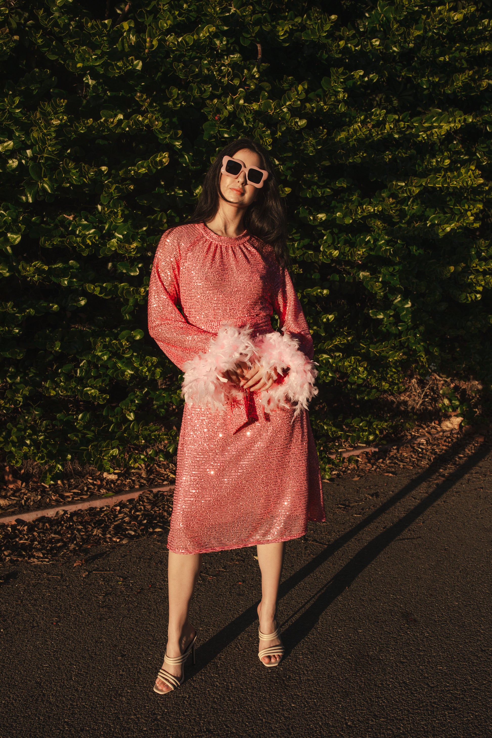 Jennafer Grace light pink flamingo sequins dress. Featuring a boat neck, generous bishop sleeves with light pink feather detail at sleeve hem, flowing midi length maxi skirt, and a slim matching sash for a cinched waist.