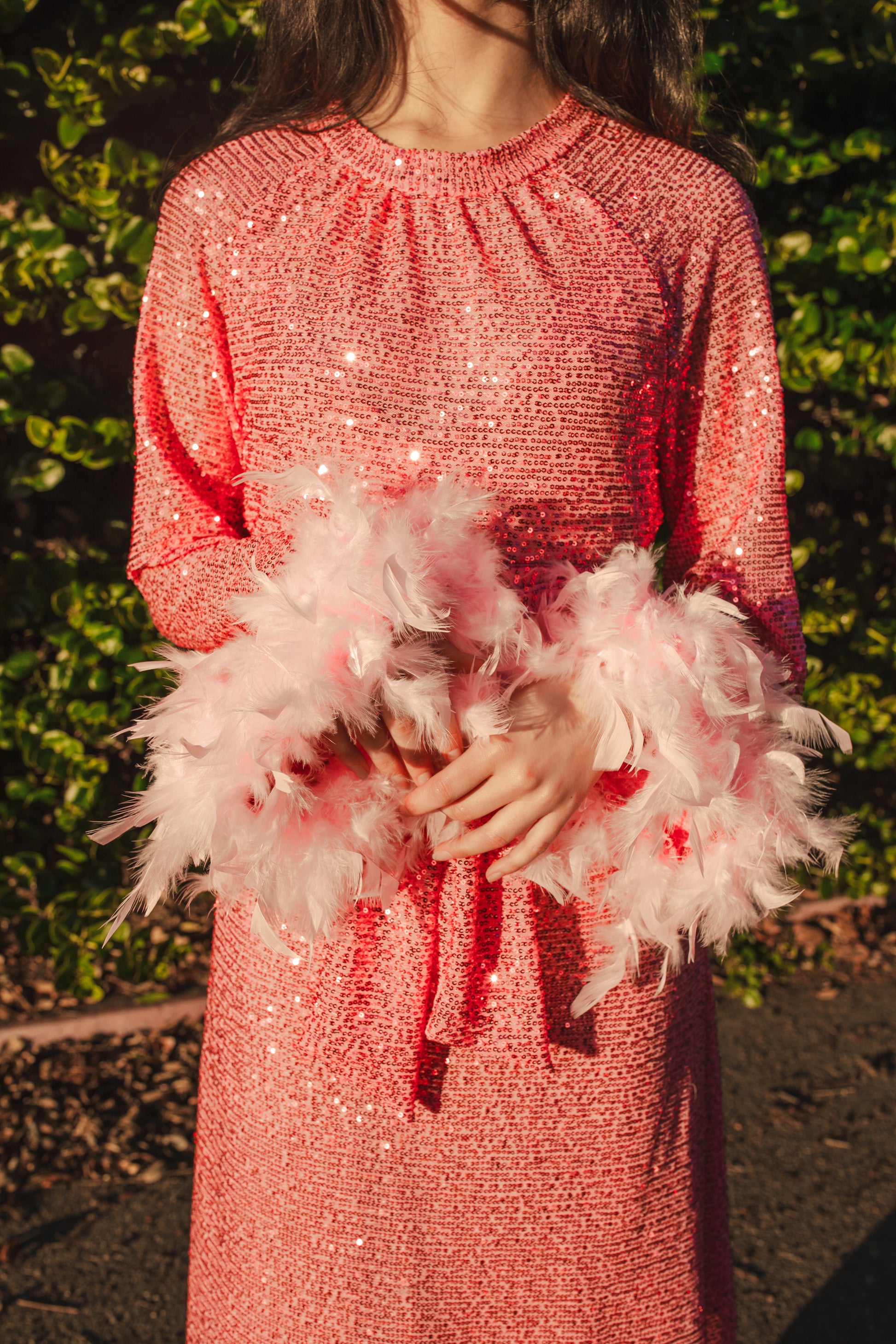 Jennafer Grace light pink flamingo sequins dress. Featuring a boat neck, generous bishop sleeves with light pink feather detail at sleeve hem, flowing midi length maxi skirt, and a slim matching sash for a cinched waist.