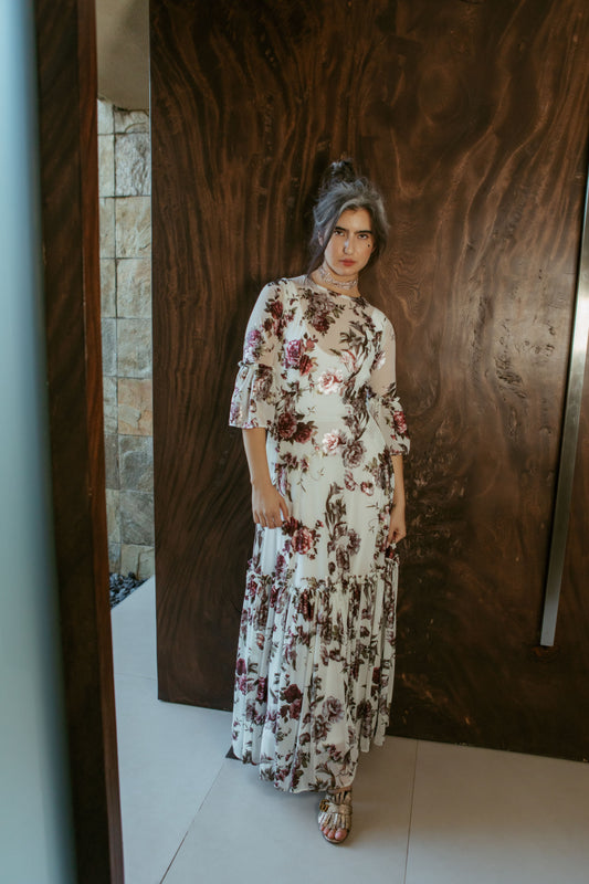 An airy ruffled maxi dress. Made with an airy and metallic detail floral mesh fabric featuring pockets, mid-length bell sleeves, and a full, single-tiered skirt with ankle hem. Includes a matching slip dress that can be worn on its own.