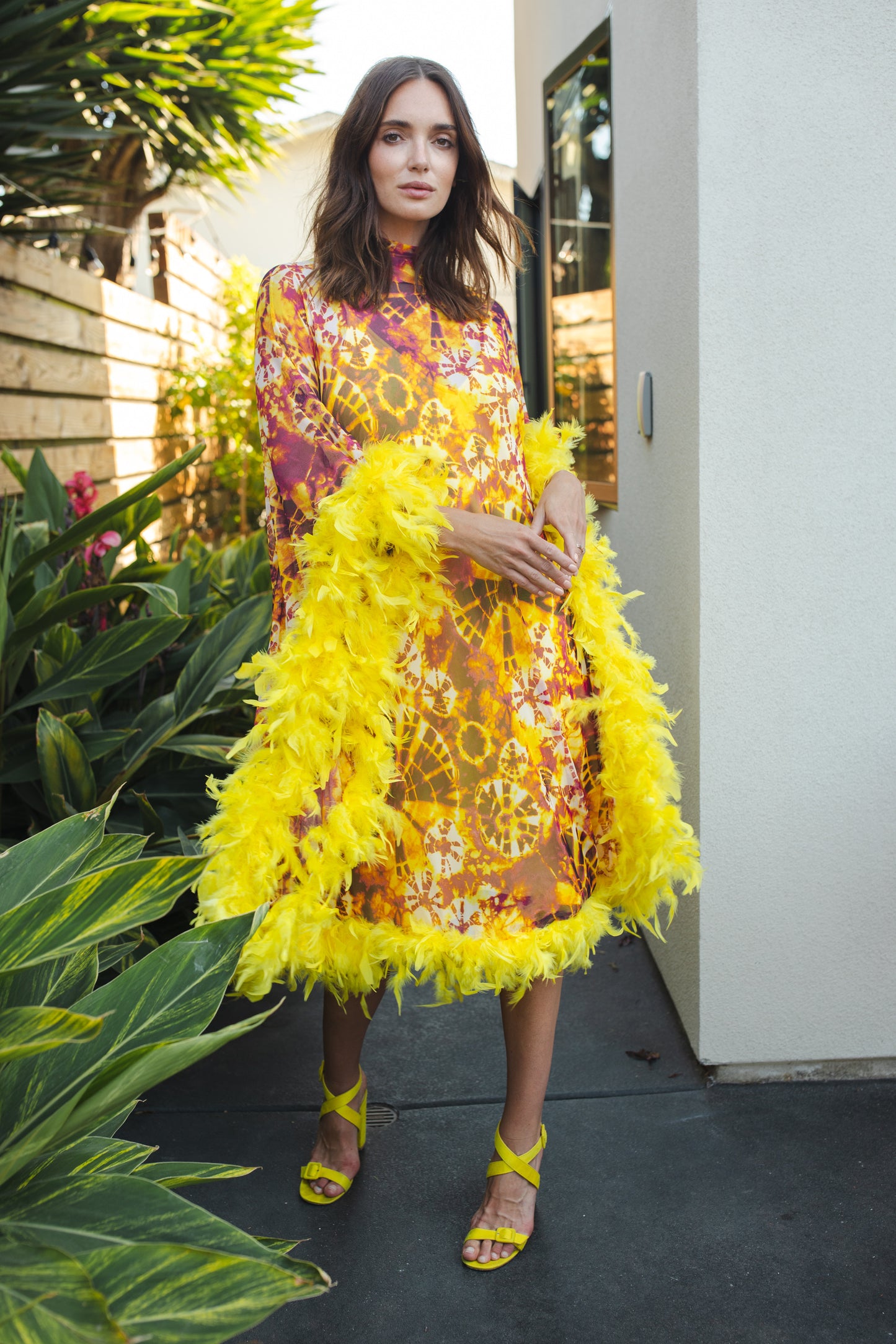 The Intra Dimensiona Mockneck Feather Caftan with slip. A vibrant, fiery abstract print featuring reds and oranges and yellows printed on a semi-sheer, super soft mesh with canary yellow feather border along sleeves and hem. A bohemian dress inspired by Old Hollywood and Palm Springs.