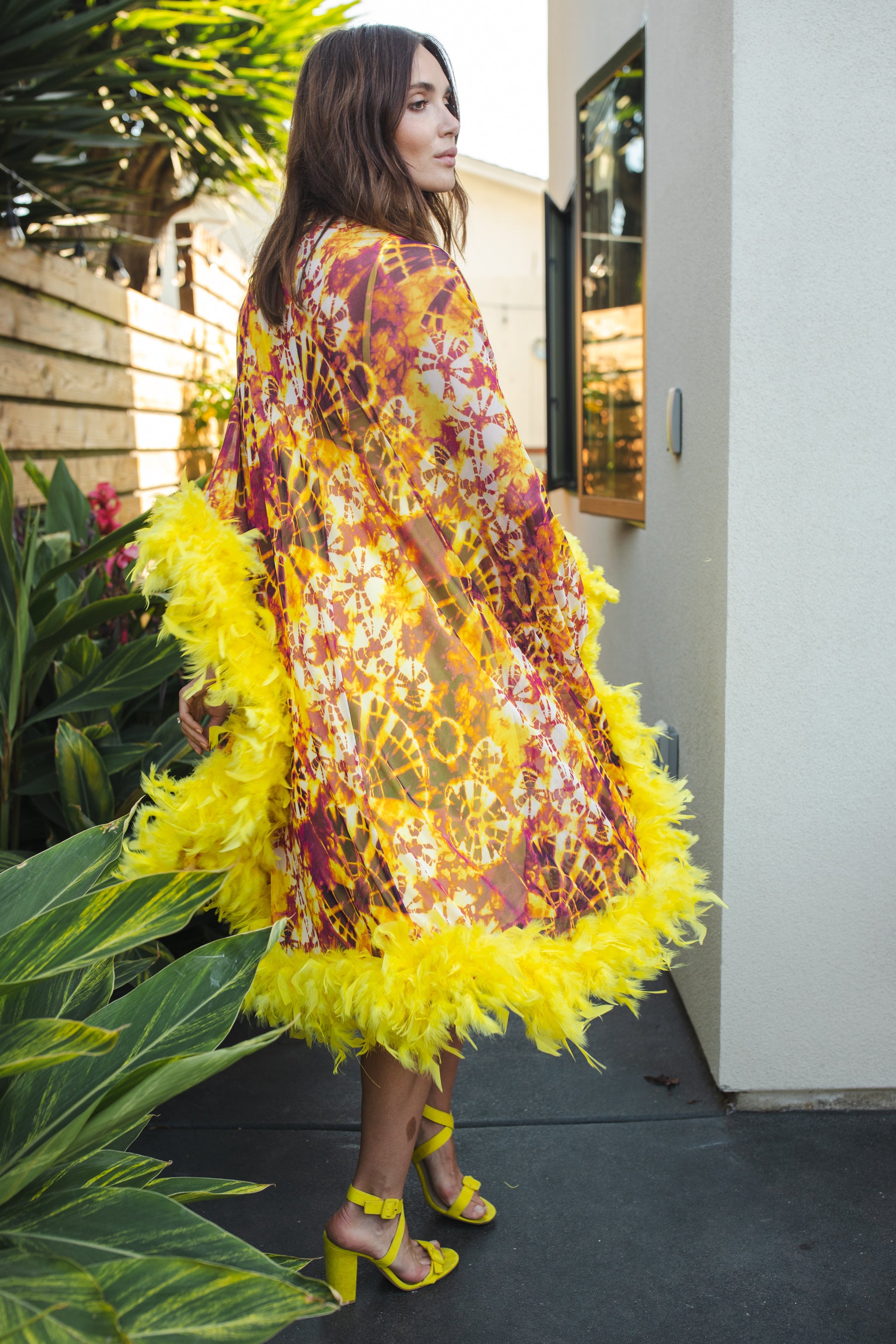 The Intra Dimensiona Mockneck Feather Caftan with slip. A vibrant, fiery abstract print featuring reds and oranges and yellows printed on a semi-sheer, super soft mesh with canary yellow feather border along sleeves and hem. A bohemian dress inspired by Old Hollywood and Palm Springs.