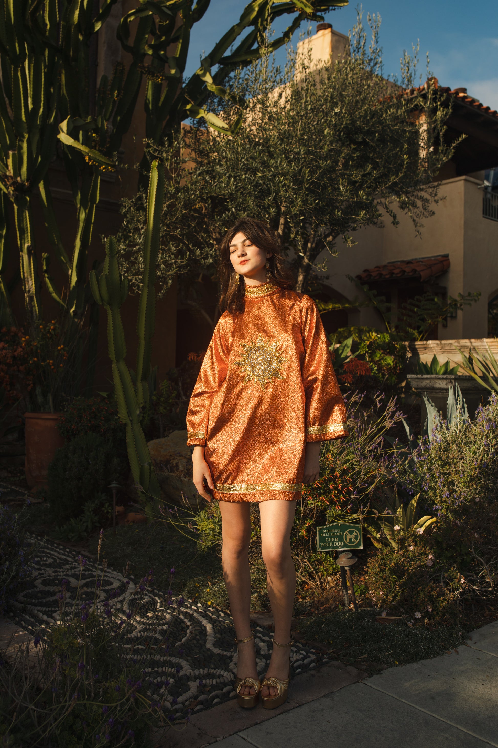 Crafted from a shimmering, fiery orange fabric embellished with an intricate sequin sun and matching sequin details at collar, cuffs, and hem, this is the bold and dreamy 60s revival romance dress every wardrobe craves