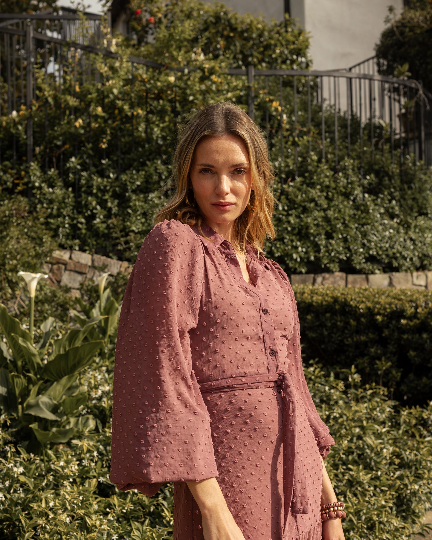 This Swiss Dot maxi dress is sophisticated yet effortless with its high collar, button-up design paired with bishop sleeves, tiered skirt, and a slim matching sash.