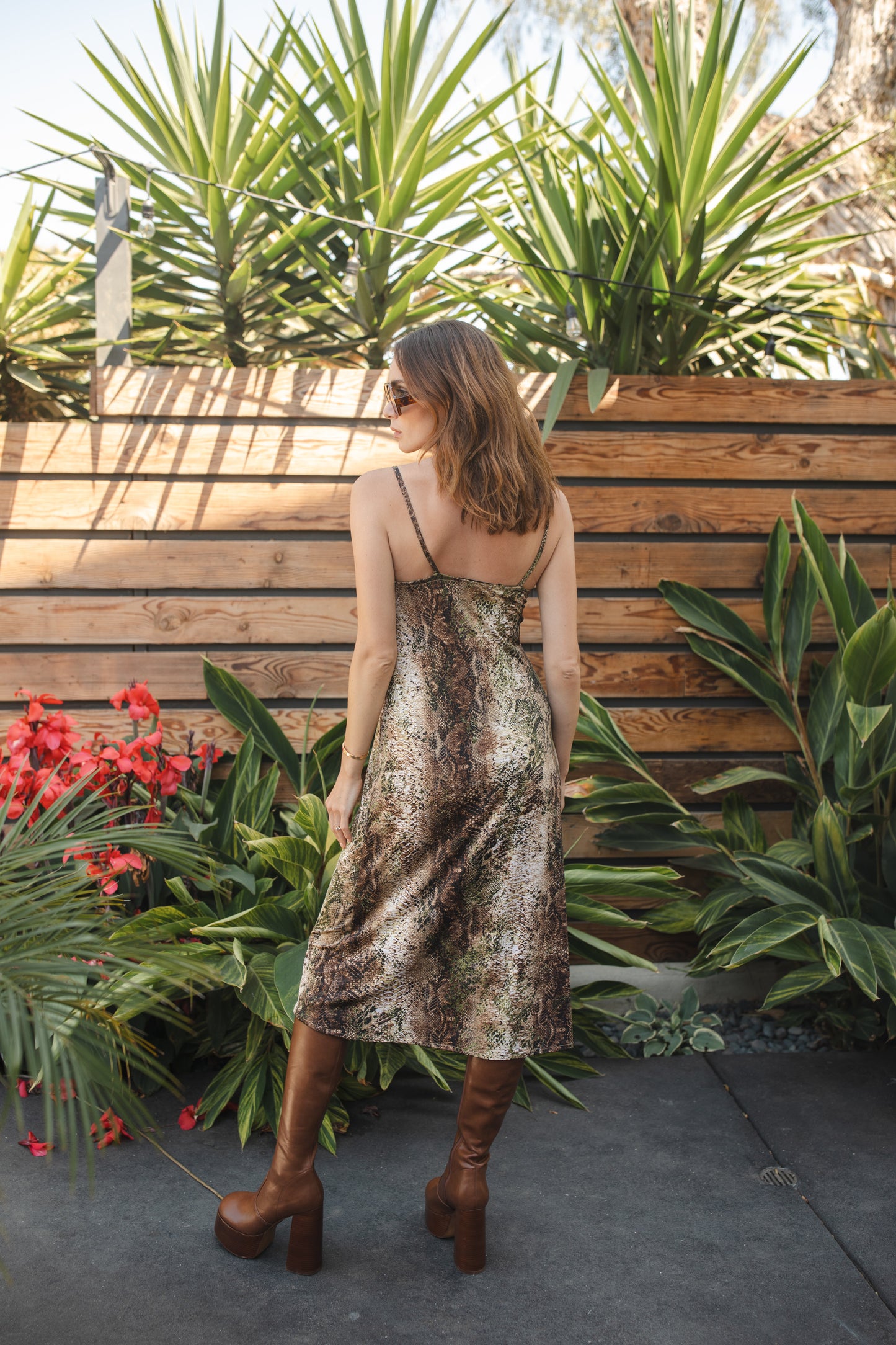 Midi slip dress with a soft beige base color, adorned with snakeskin pattern featuring shades of green and brown. It features slender straps with a straight silhouette and relaxed fix, allowing for a beautiful drape and flowy movement. It's designed for a light, airy feel, suitable for warm weather or layered for cooler days.