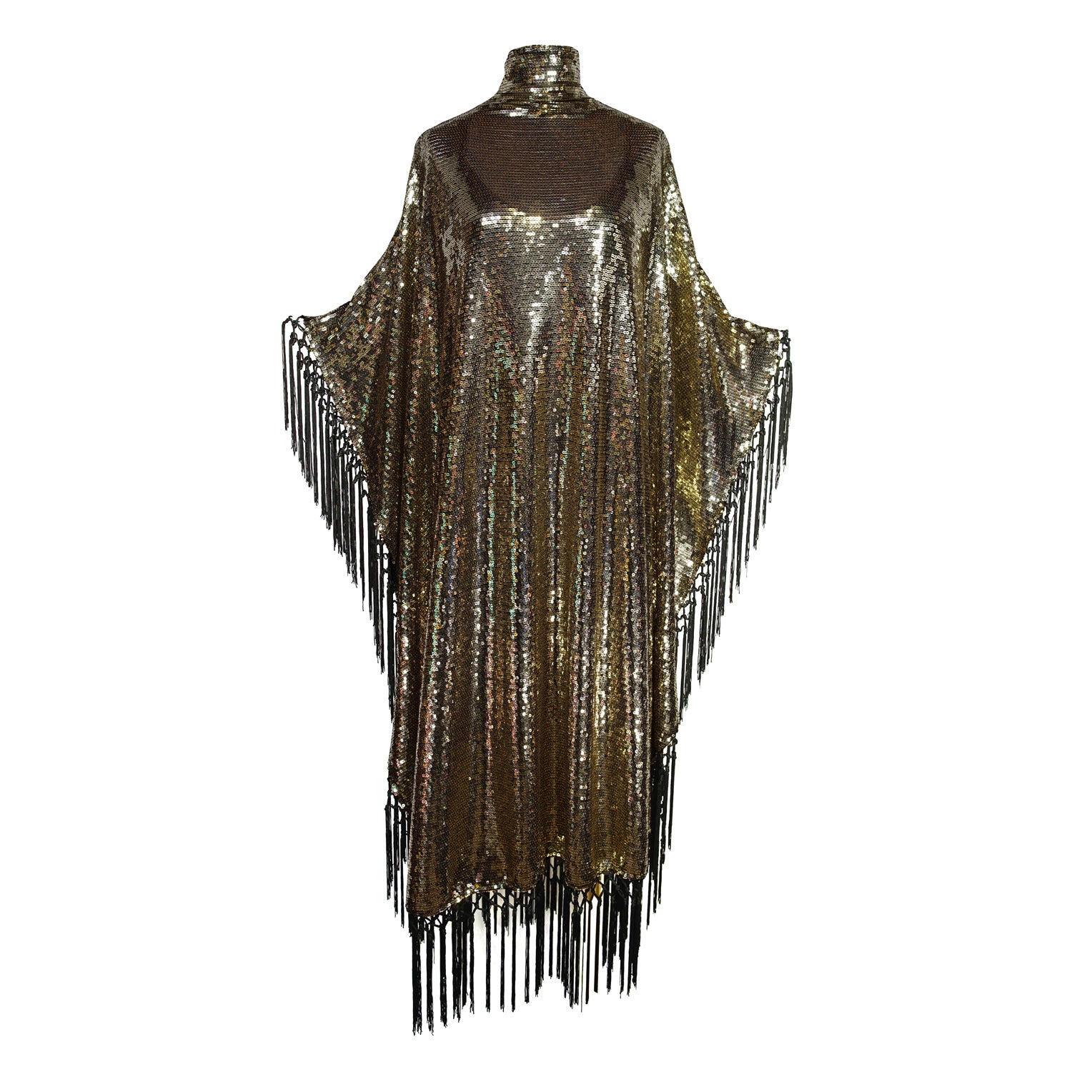 This caftan is a dazzling, full-length garment featuring a shimmering gold sequin overlay on a mesh fabric. The sequins catch the light, creating a sparkling effect throughout. It has a mock neck collar with a straight, loose fit that drapes elegantly over the body. The edges of the caftan, including the hem and the sides, are embellished with long, silk black fringe that add movement and a playful flair to the garment.