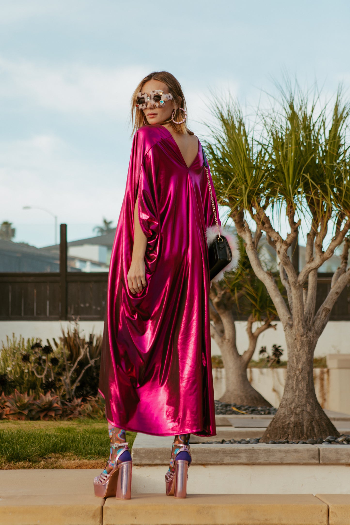 Bold, metallic caftan crafted from a slinky black jersey coated with a deep fuchsia foil that shimmers in the light. The caftan has a generous, free-flowing cut, with ample fabric creating an elegant, loose fit that drapes comfortably over the body, with batwing sleeves and a deep v-neckline.