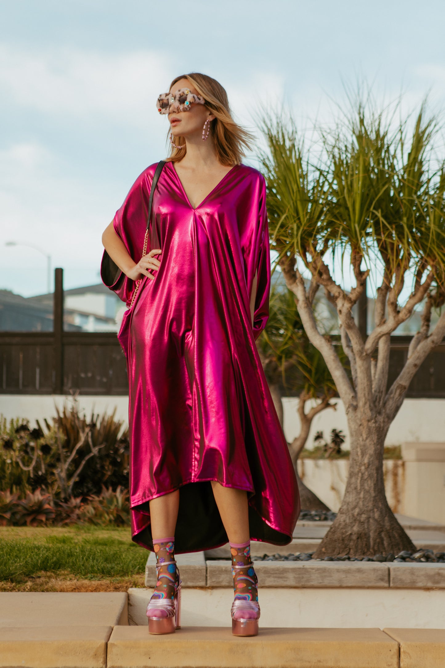 Bold, metallic caftan crafted from a slinky black jersey coated with a deep fuchsia foil that shimmers in the light. The caftan has a generous, free-flowing cut, with ample fabric creating an elegant, loose fit that drapes comfortably over the body, with batwing sleeves and a deep v-neckline.