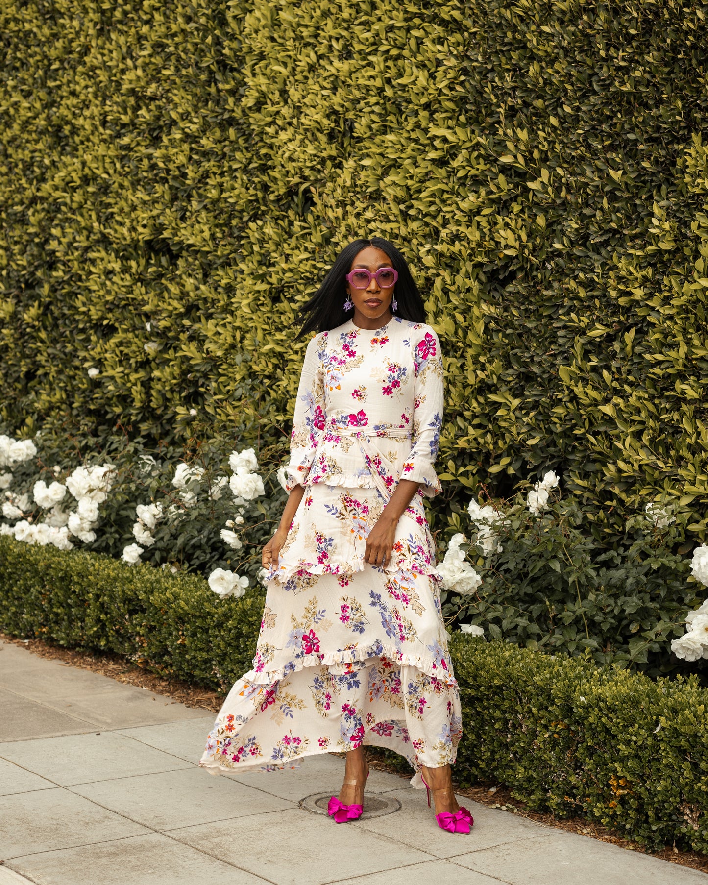 A floral maxi dress made from a soft, linen like crepe, it features high neck, bishop sleeves, tiered ruffle skirt and matching sash for a cinched waist. It's light, airy silhouette. Base color is pale yellow with a mixture of fuchsia, orange, and blue flowers as the print.
