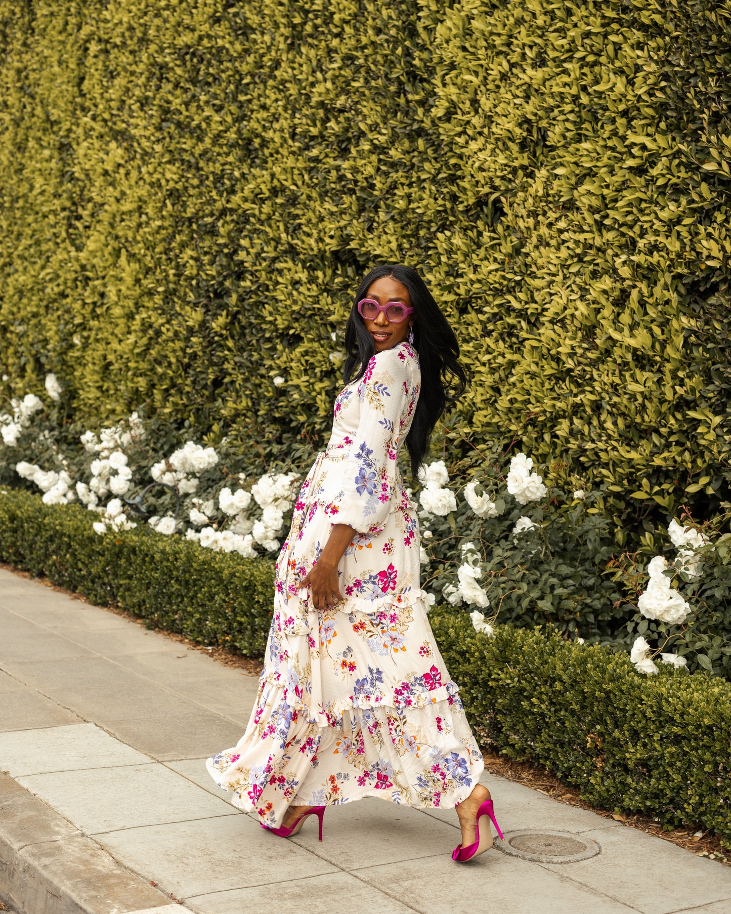 A floral maxi dress made from a soft, linen like crepe, it features high neck, bishop sleeves, tiered ruffle skirt and matching sash for a cinched waist. It's light, airy silhouette. Base color is pale yellow with a mixture of fuchsia, orange, and blue flowers as the print.