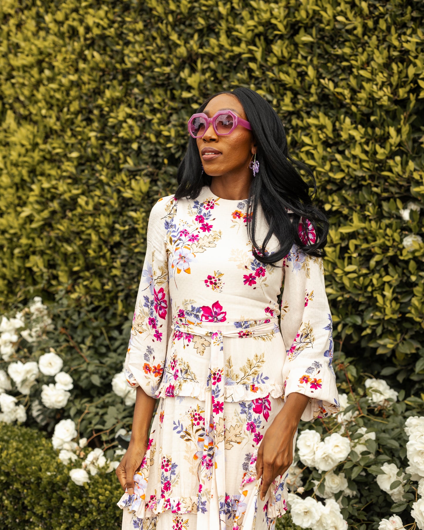 A floral maxi dress made from a soft, linen like crepe, it features high neck, bishop sleeves, tiered ruffle skirt and matching sash for a cinched waist. It's light, airy silhouette. Base color is pale yellow with a mixture of fuchsia, orange, and blue flowers as the print.