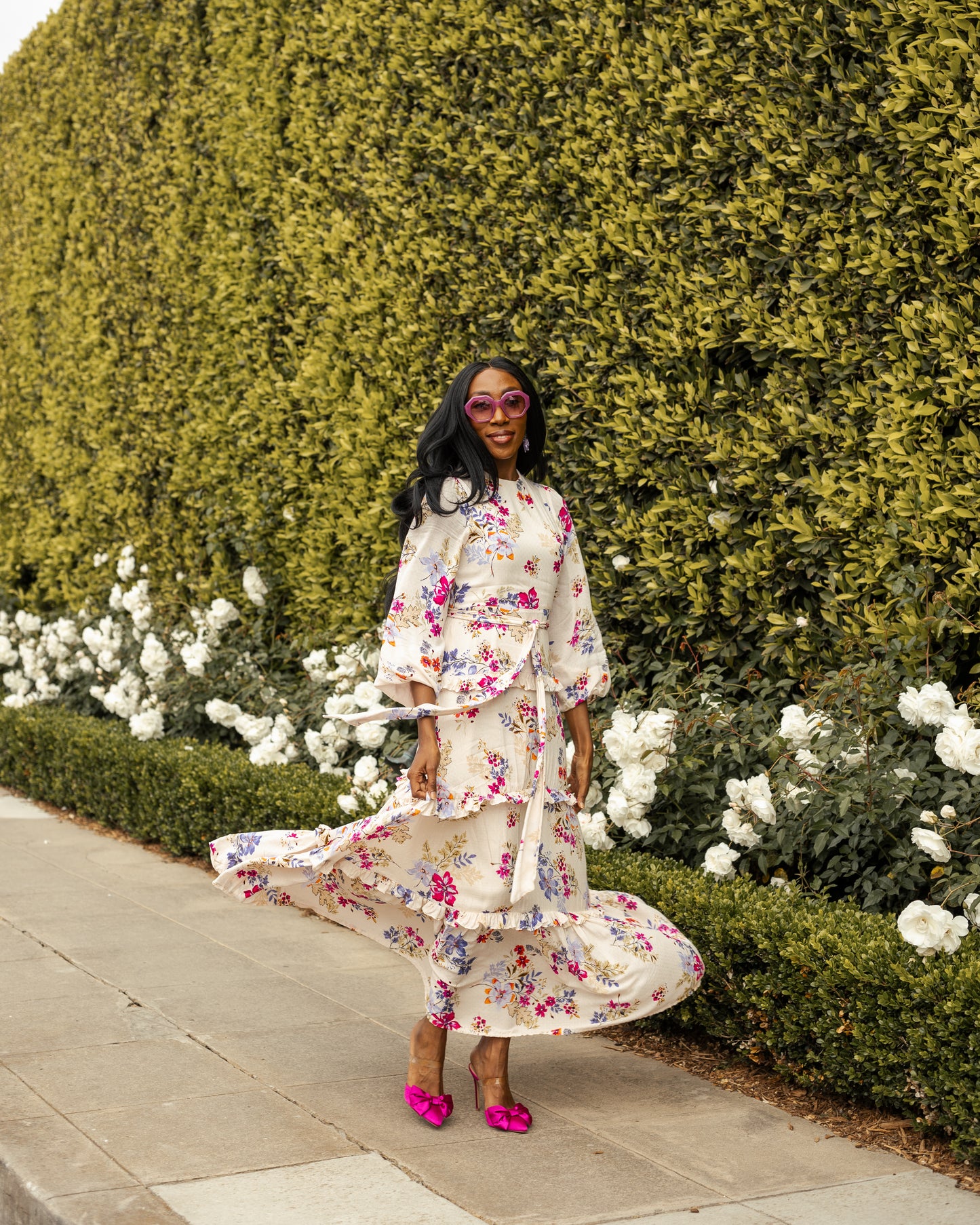 A floral maxi dress made from a soft, linen like crepe, it features high neck, bishop sleeves, tiered ruffle skirt and matching sash for a cinched waist. It's light, airy silhouette. Base color is pale yellow with a mixture of fuchsia, orange, and blue flowers as the print.