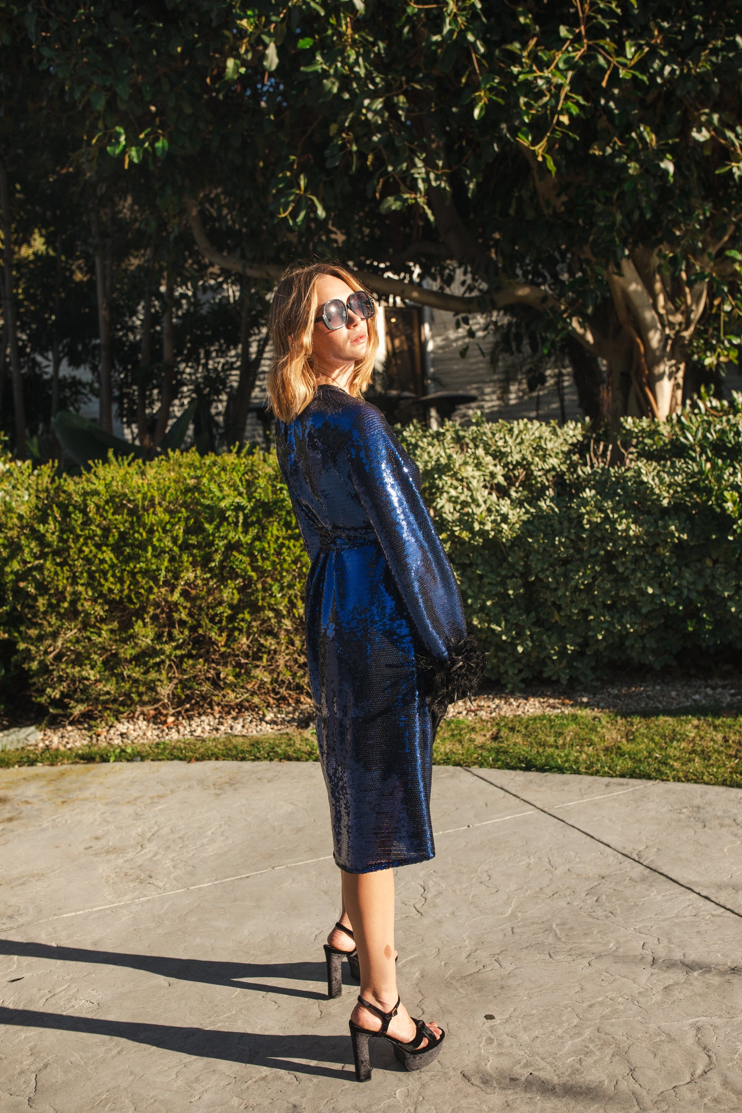 Model wears a knee length dress covered in midnight blue sequins, the dress has a crew neck and full long sleeves with a feather trim.