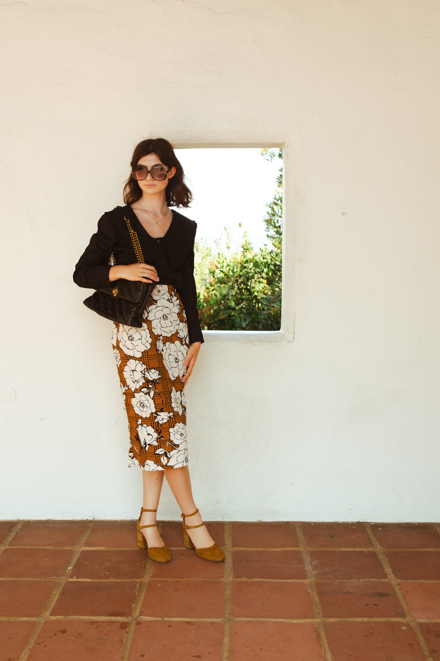 Cognac brown midi pencil skirt featuring black houndstooth pattern overlaid with large, modern, white and black floral print. This skirt is below the knee in length with an elastic waist for comfort. Bohemian floral meets dark academia in style.