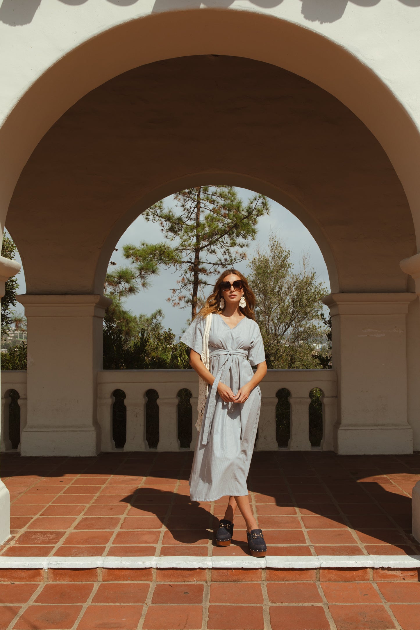 White and blue vertical pinstripe a-line midi-maxi dress featuring v-neck, short sleeves, and built-in sash ties for a cinched, wrap waist look. This dress falls at approximately lower calf or ankle. Nautical bohemian in style.