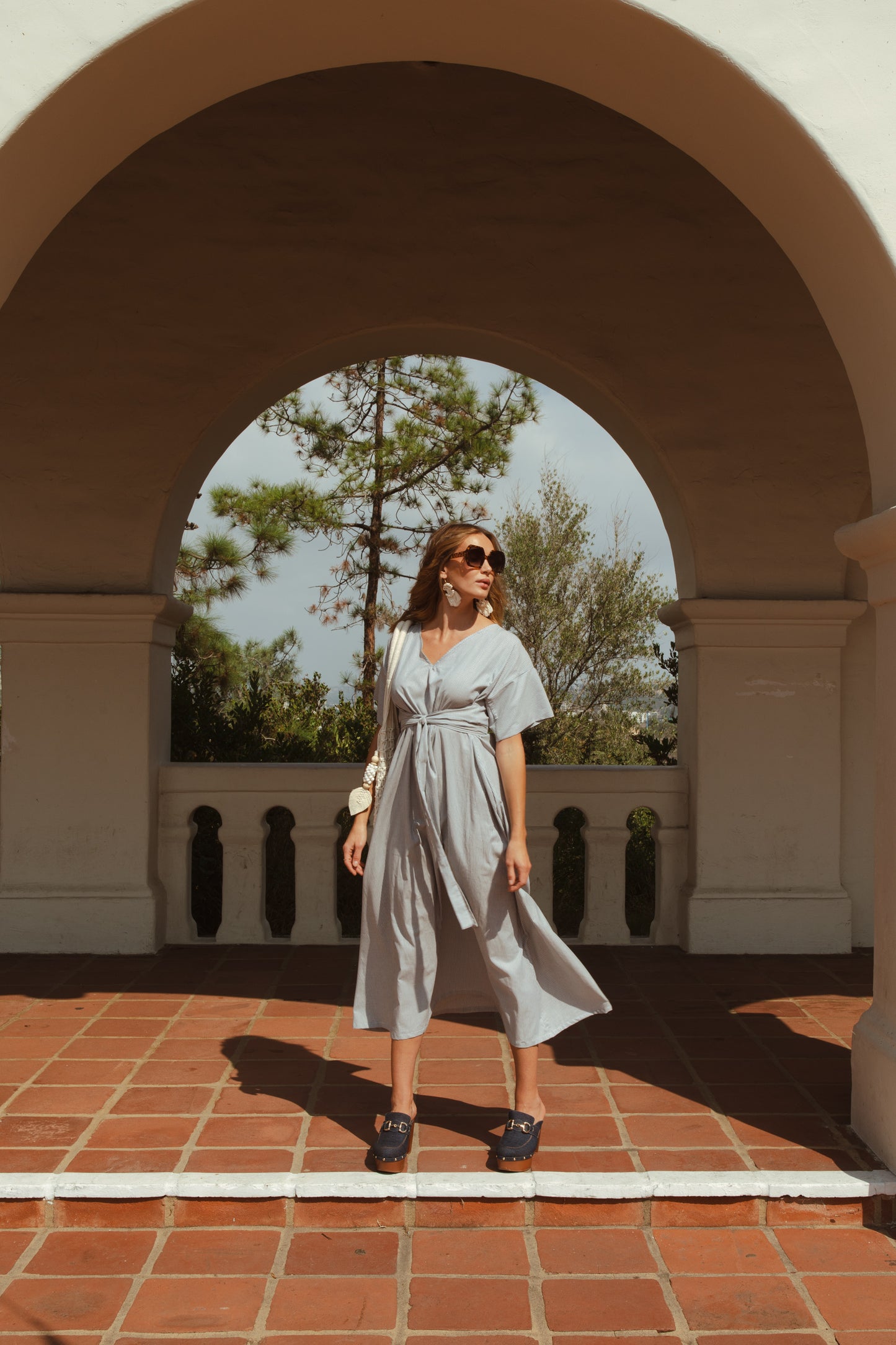 White and blue vertical pinstripe a-line midi-maxi dress featuring v-neck, short sleeves, and built-in sash ties for a cinched, wrap waist look. This dress falls at approximately lower calf or ankle. Nautical bohemian in style.