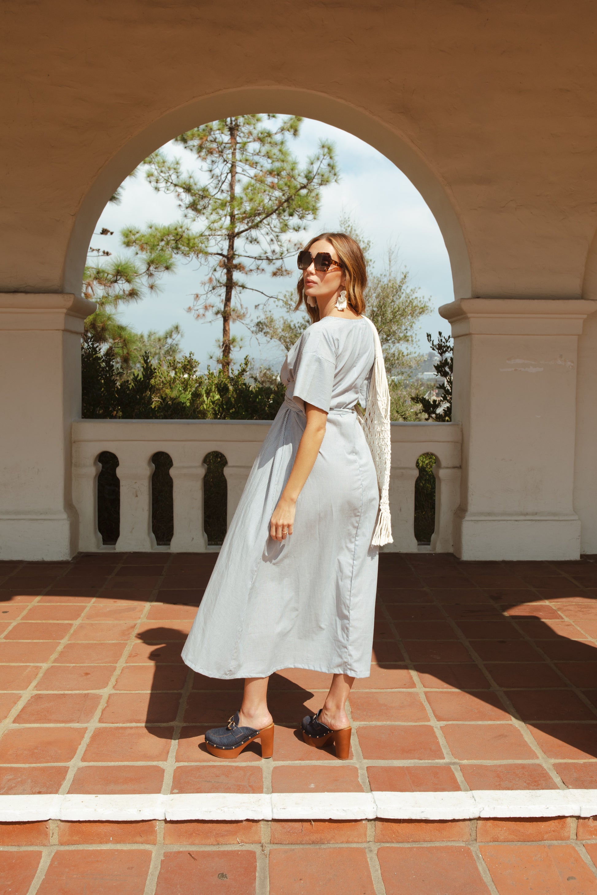 White and blue vertical pinstripe a-line midi-maxi dress featuring v-neck, short sleeves, and built-in sash ties for a cinched, wrap waist look. This dress falls at approximately lower calf or ankle. Nautical bohemian in style.