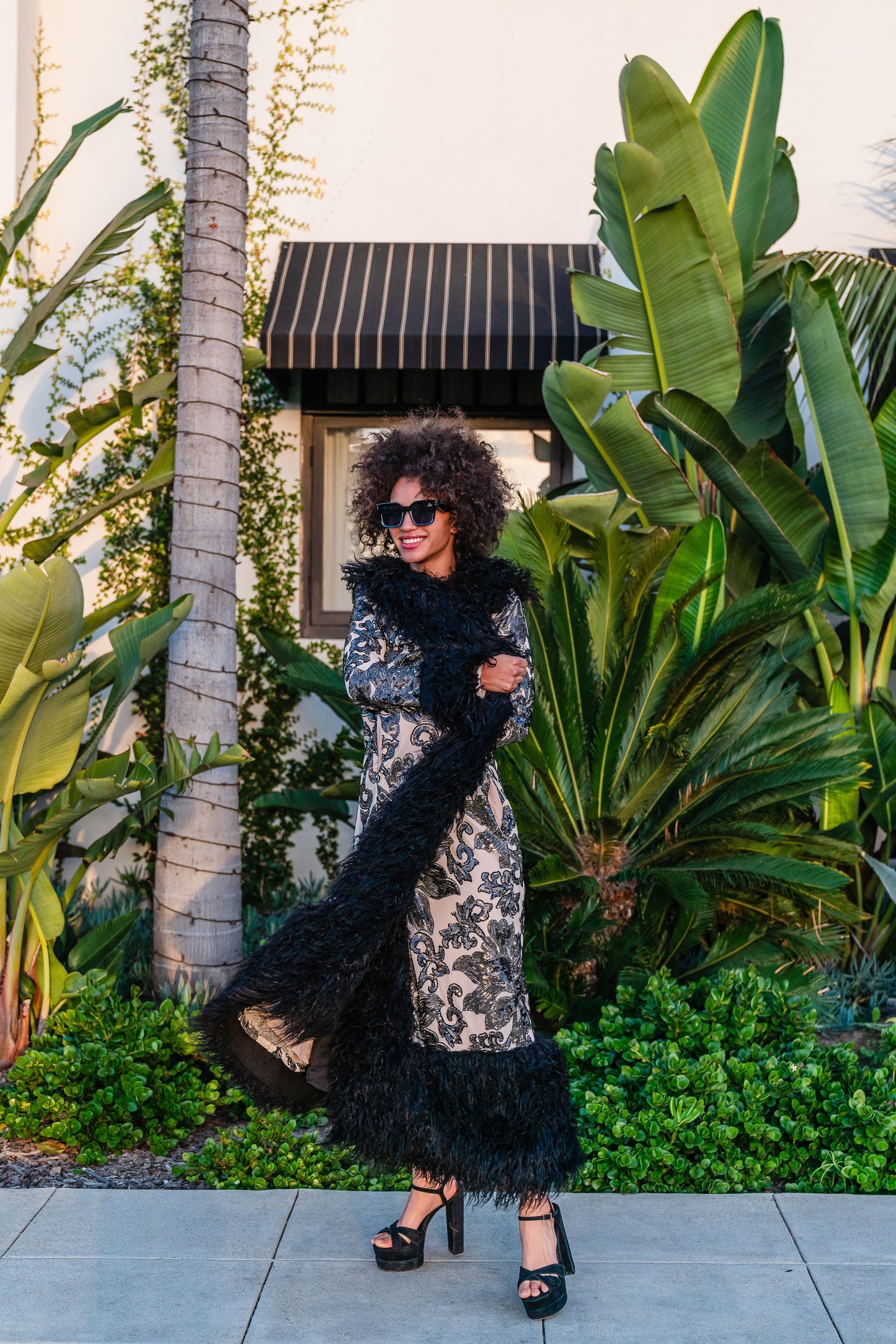 A floor length coat made of nude mesh with black sequins in a floral patter. The coat is lined around the collar, down the opening and around the hem in fluffy black faux alpaca fur, the coat has pockets and a nude colored lining of bamboo jersey.