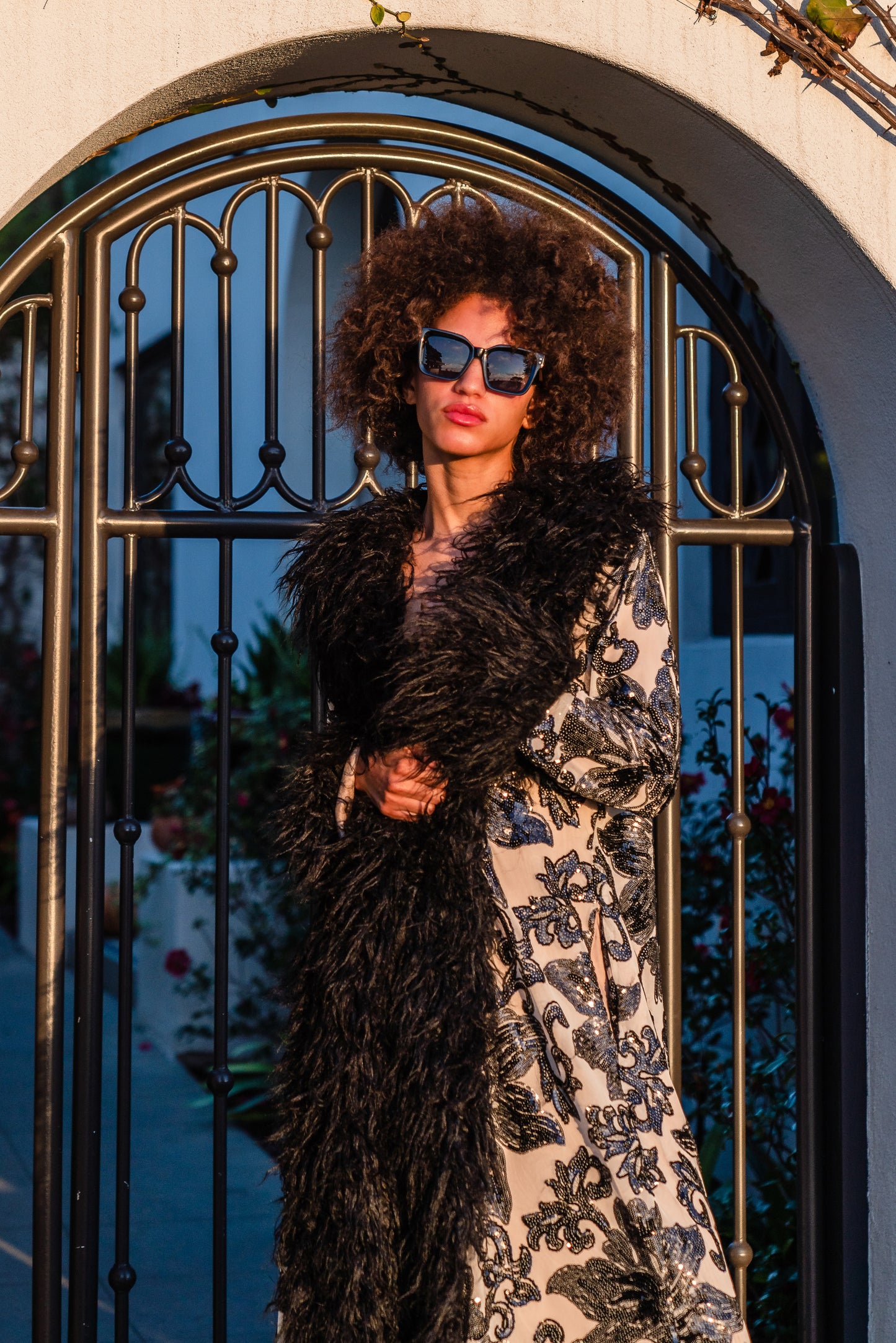 A floor length coat made of nude mesh with black sequins in a floral patter. The coat is lined around the collar, down the opening and around the hem in fluffy black faux alpaca fur, the coat has pockets and a nude colored lining of bamboo jersey.