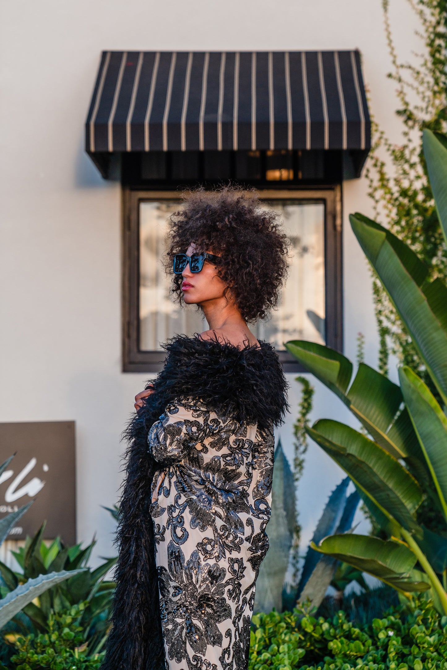 A floor length coat made of nude mesh with black sequins in a floral patter. The coat is lined around the collar, down the opening and around the hem in fluffy black faux alpaca fur, the coat has pockets and a nude colored lining of bamboo jersey.