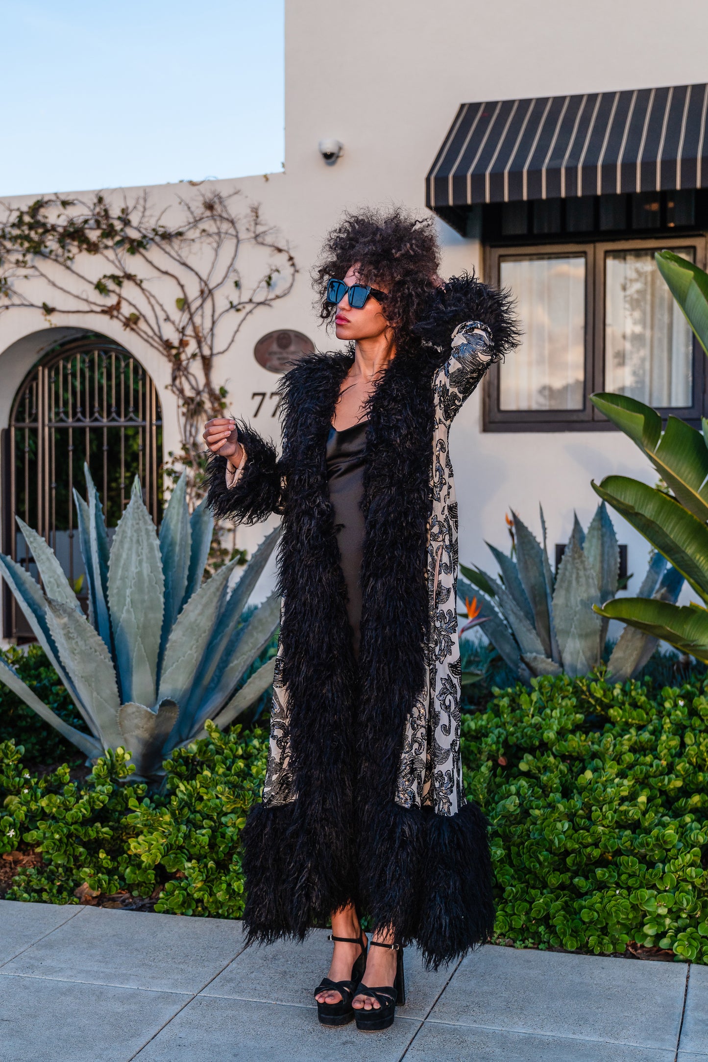 A floor length coat made of nude mesh with black sequins in a floral patter. The coat is lined around the collar, down the opening and around the hem in fluffy black faux alpaca fur, the coat has pockets and a nude colored lining of bamboo jersey.