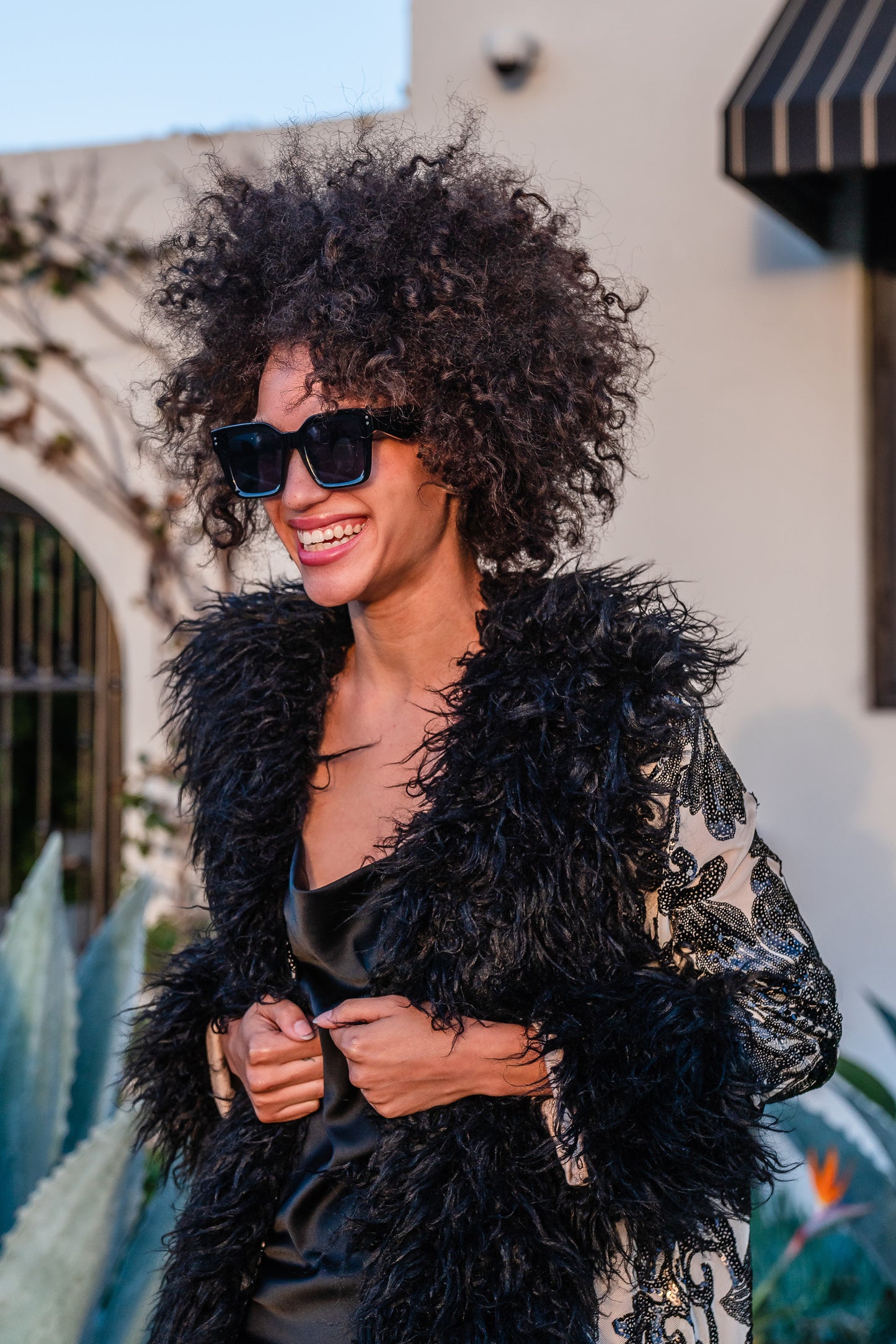 A floor length coat made of nude mesh with black sequins in a floral patter. The coat is lined around the collar, down the opening and around the hem in fluffy black faux alpaca fur, the coat has pockets and a nude colored lining of bamboo jersey.