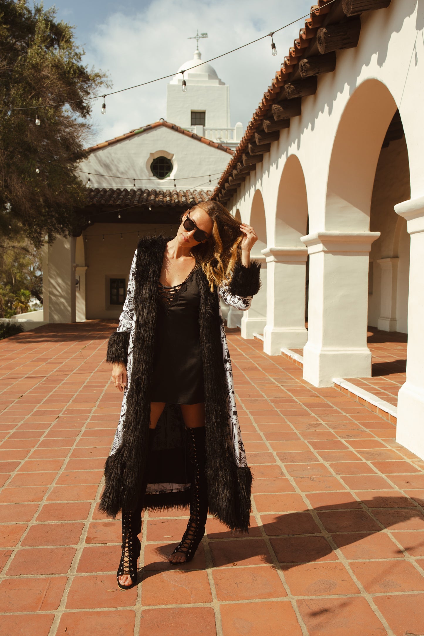 Long, penny lane style trench coat fashioned from an ivory white fabric overlaid with anatomical skeleton sketches. Embellished with long, black faux fur along collar, lapel, cuffs, and hem. High contrast black and white, spooky gothic aesthetic mixed with retro 70s style.