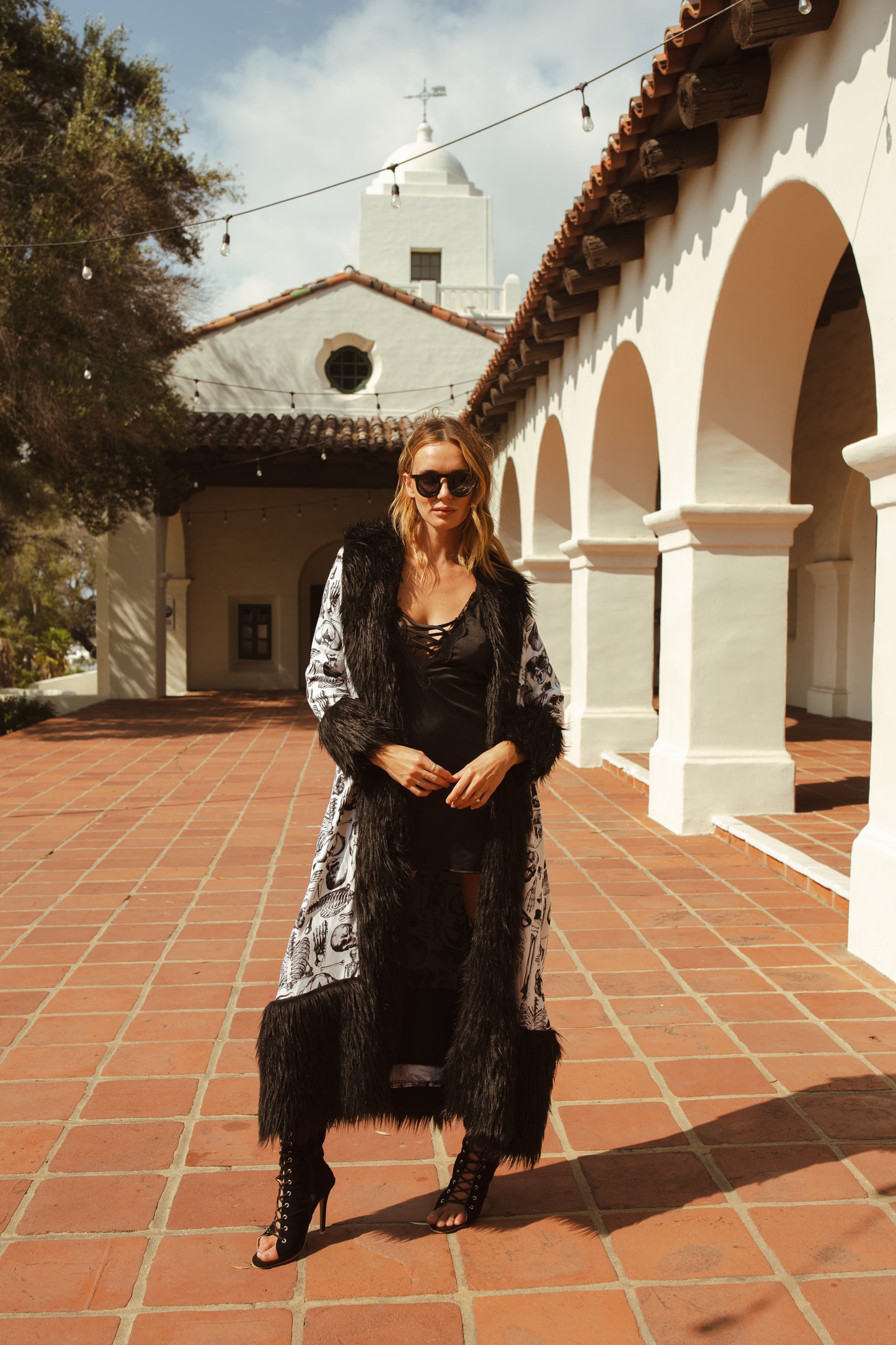 Long, penny lane style trench coat fashioned from an ivory white fabric overlaid with anatomical skeleton sketches. Embellished with long, black faux fur along collar, lapel, cuffs, and hem. High contrast black and white, spooky gothic aesthetic mixed with retro 70s style.