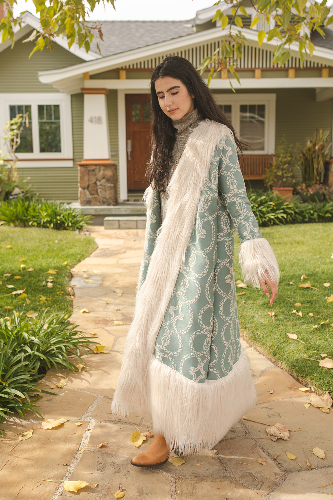 Long, penny lane style trench coat fashioned from a thick, mint green fabric embroidered with ivory snakes. Embellished with long ivory faux fur along collar, lapel, cuffs, and hem. Bohemian maximalism in style.