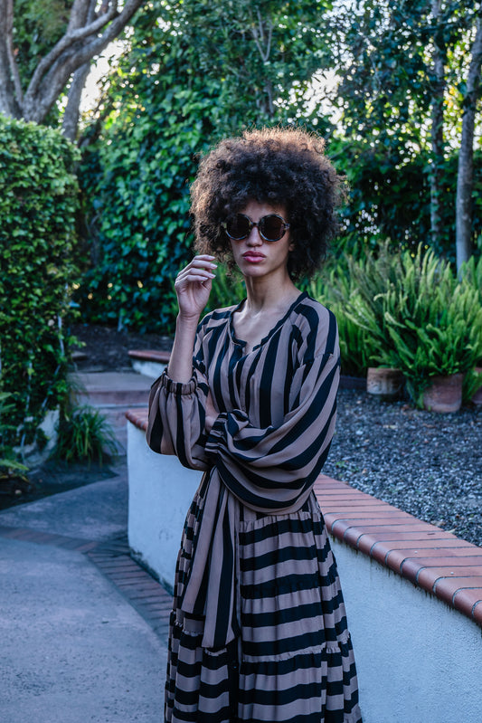 A coffee colored striped ruffled maxi dress. Featuring thick black and brown café stripes, long sleeves, ankle hem, full length button down in front, and optional belt to cinch the waist.