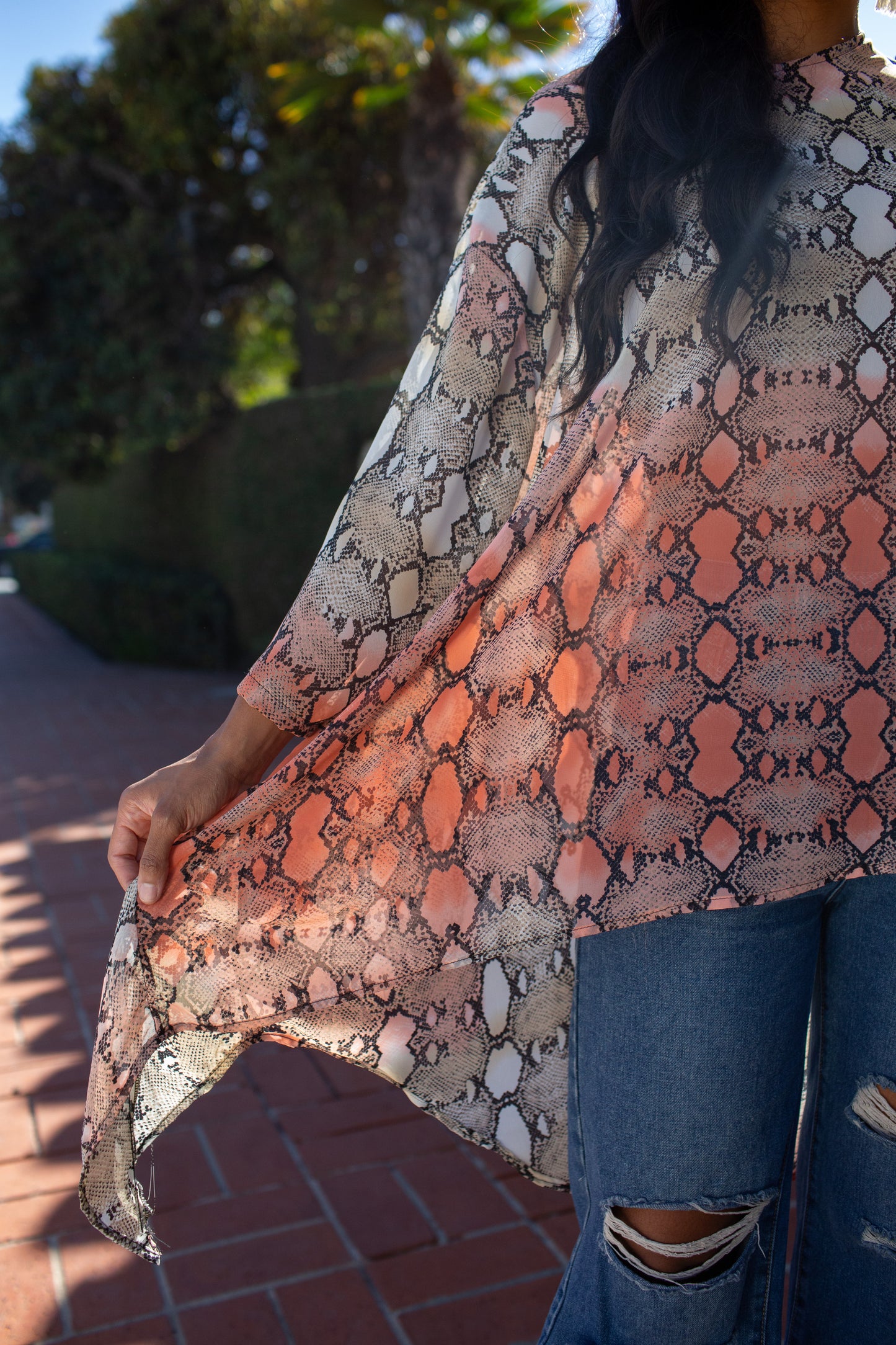 This orange and turquoise snakeskin print top features a wide boat neckline, gracefully exposing the collarbone, while batwing sleeves extend from the shoulders, flowing freely like a soft cascade of fabric. The waist-length hem adds a touch of structure, making it versatile for styling.