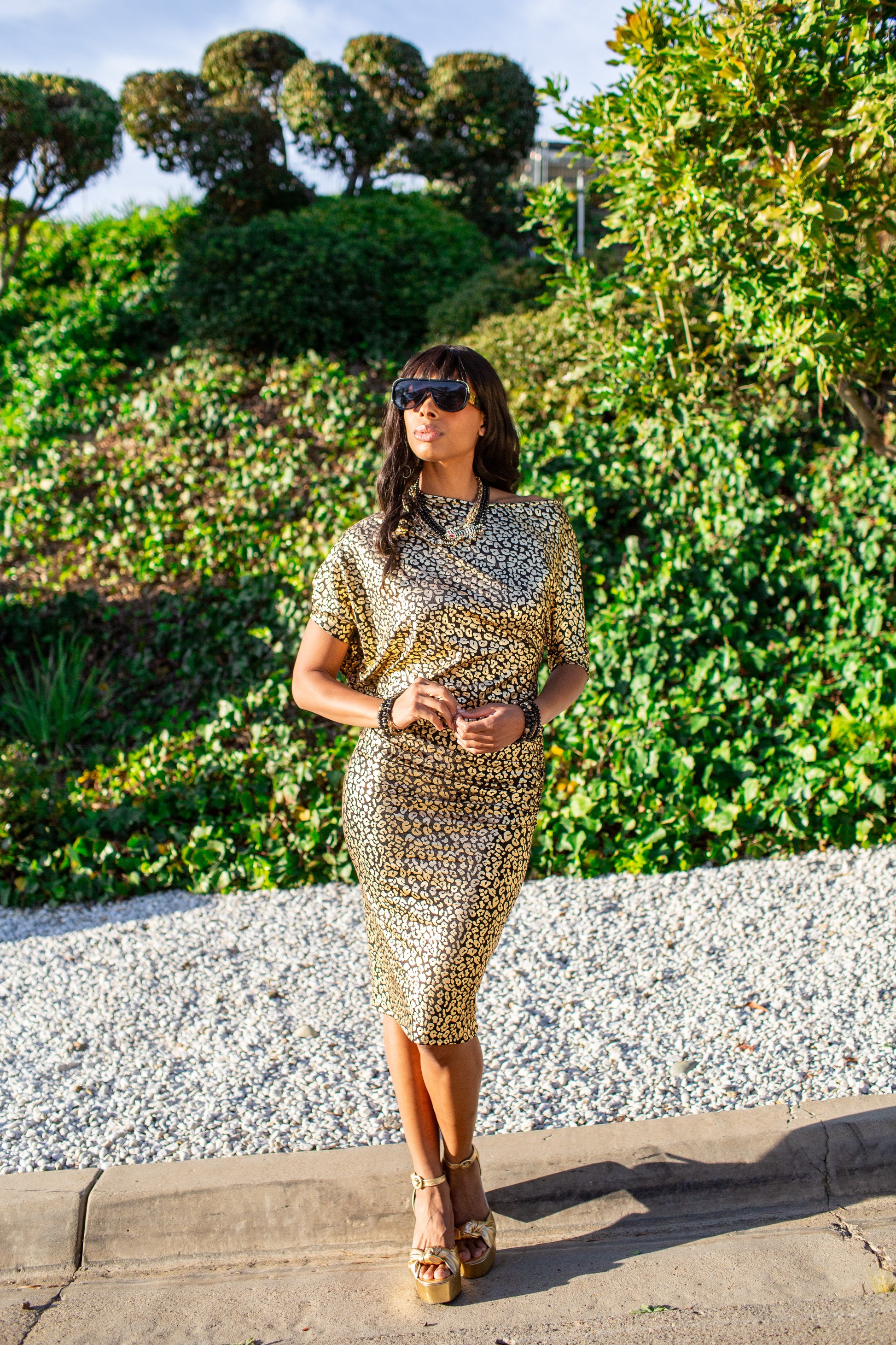 An angle dress made from a gold leopard foil-detailed stretchy jersey, featuring a fitted pencil skirt and light ruching at the hip. The angled sleeves can be arranged for a peek of shoulder and bra strap.